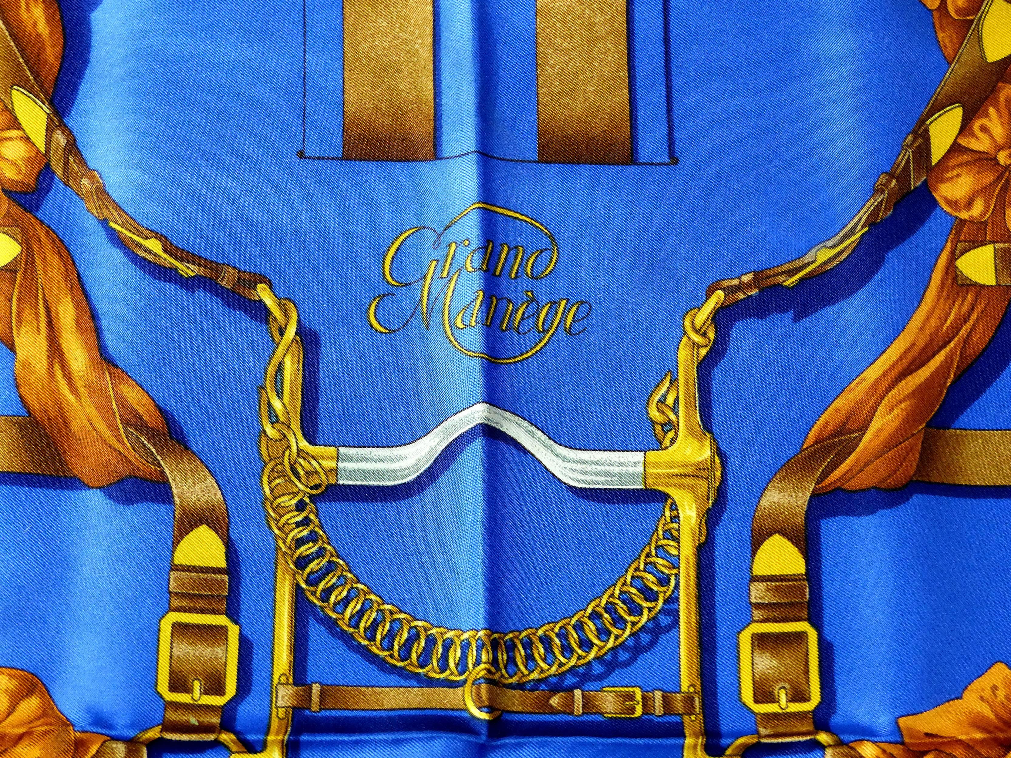 Offered for sale is blue silk equestrian theme scarf title "Grand Manege" designed by Henri d'Origny for Hermes in 1990. The design involves bridles and saddles with bits and sturrips  The scarf is unused as it was acquired from a