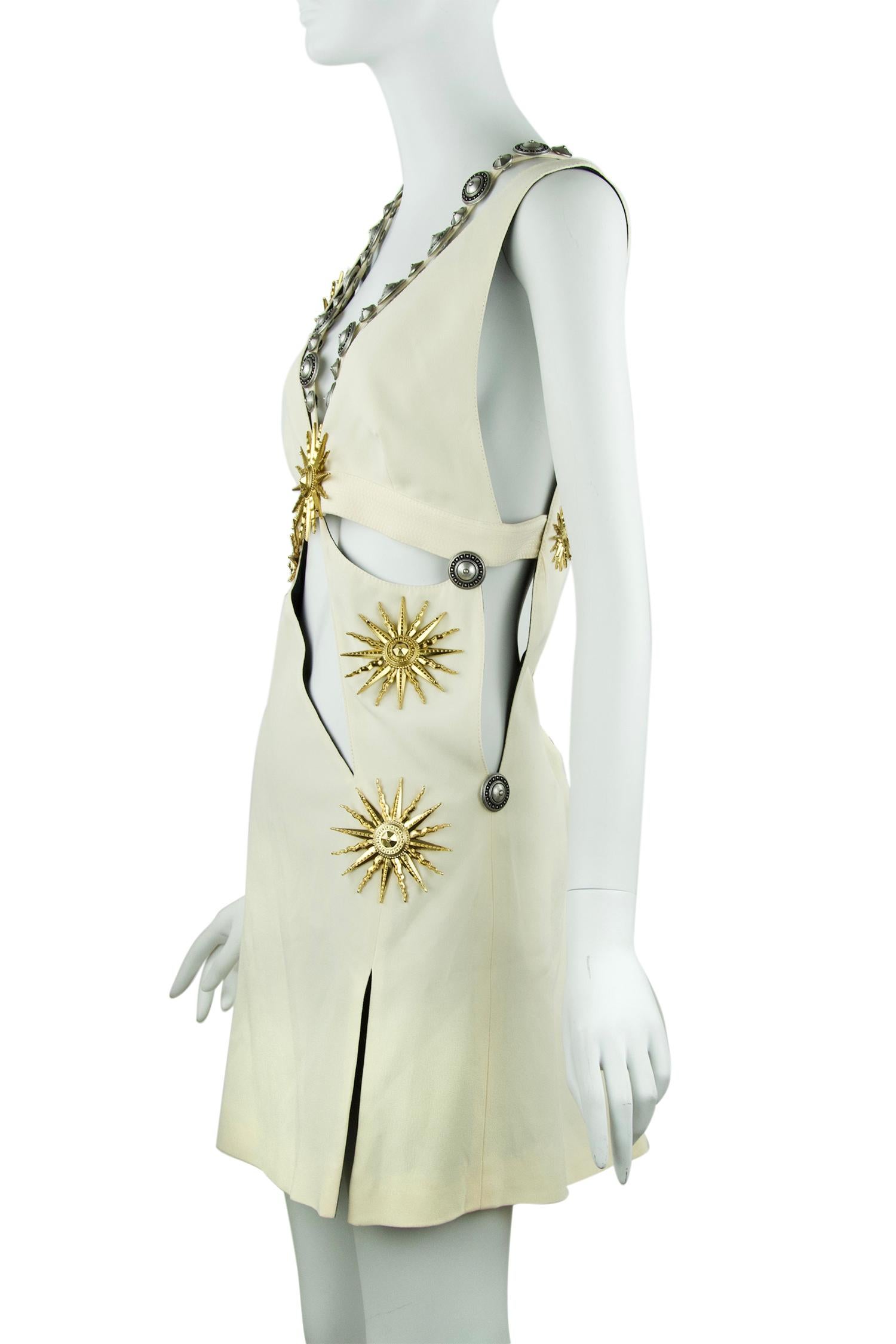 Sexy off white mini dress with asymmetrical cut outs and gold sun medallions scattered throughout.  Features a sheath silhouette and funky double straps with large silver balls.

Size: IT 42

Condition: New with tags

Composition: 79% acetate, 21%