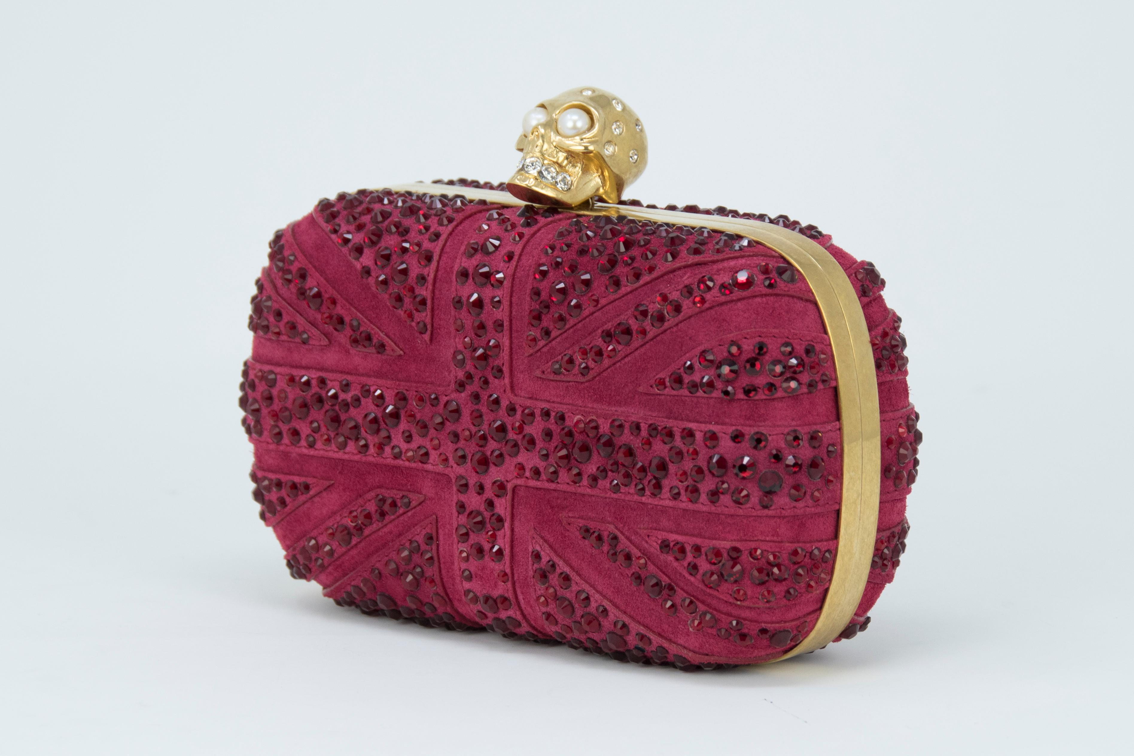 Alexander McQueen Britannia Skull Box Clutch in dark red suede Union Jack flag inspired design with signature gold skull hardware with rhinestone and pearl embellishments.

Condition: New condition

Dimensions (Approximate): 3.9