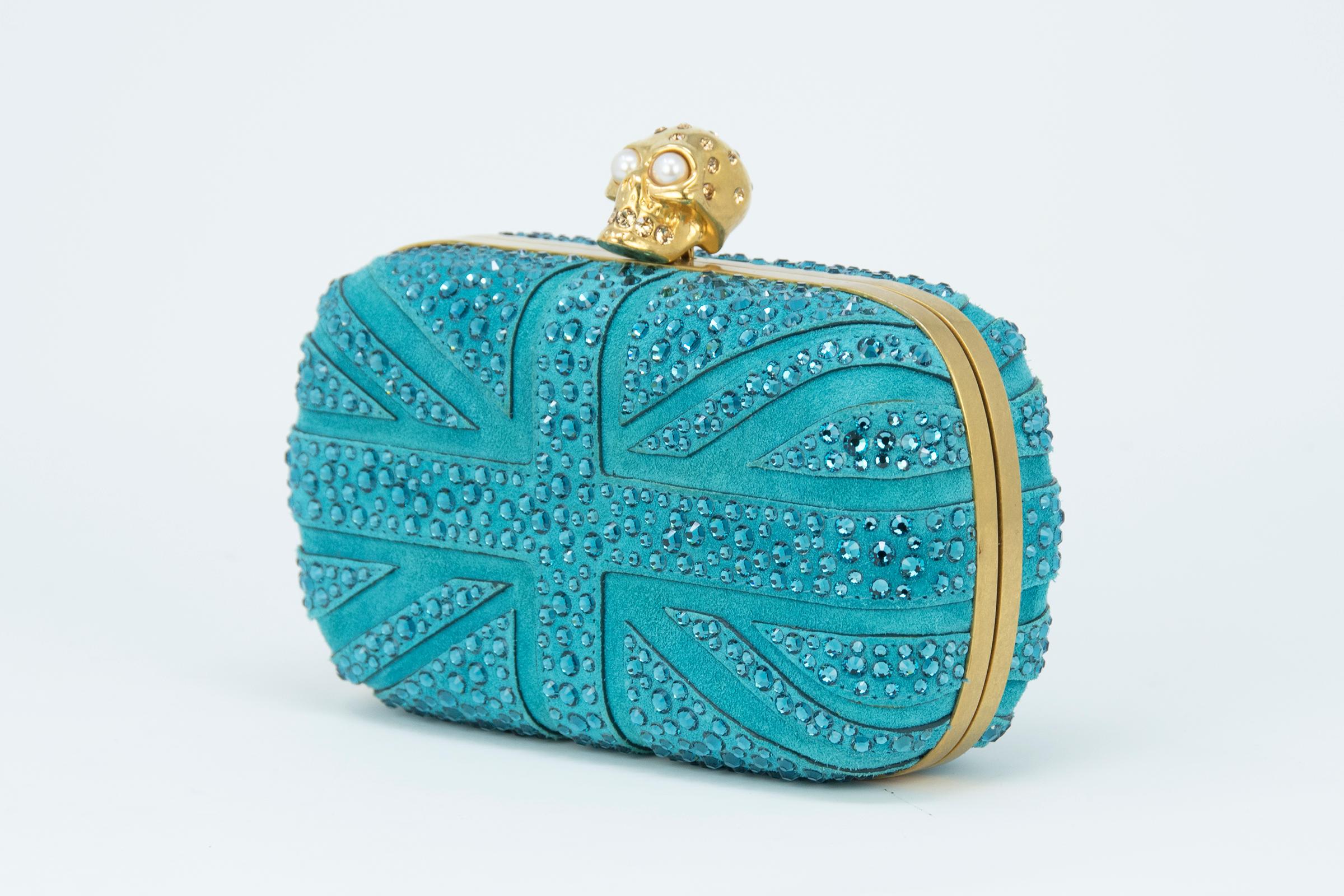 Alexander McQueen Britannia Skull Box Clutch in blue suede Union Jack flag inspired design with signature gold skull hardware with rhinestone and pearl embellishments.

Condition: New condition

Dimensions (Approximate): 3.9
