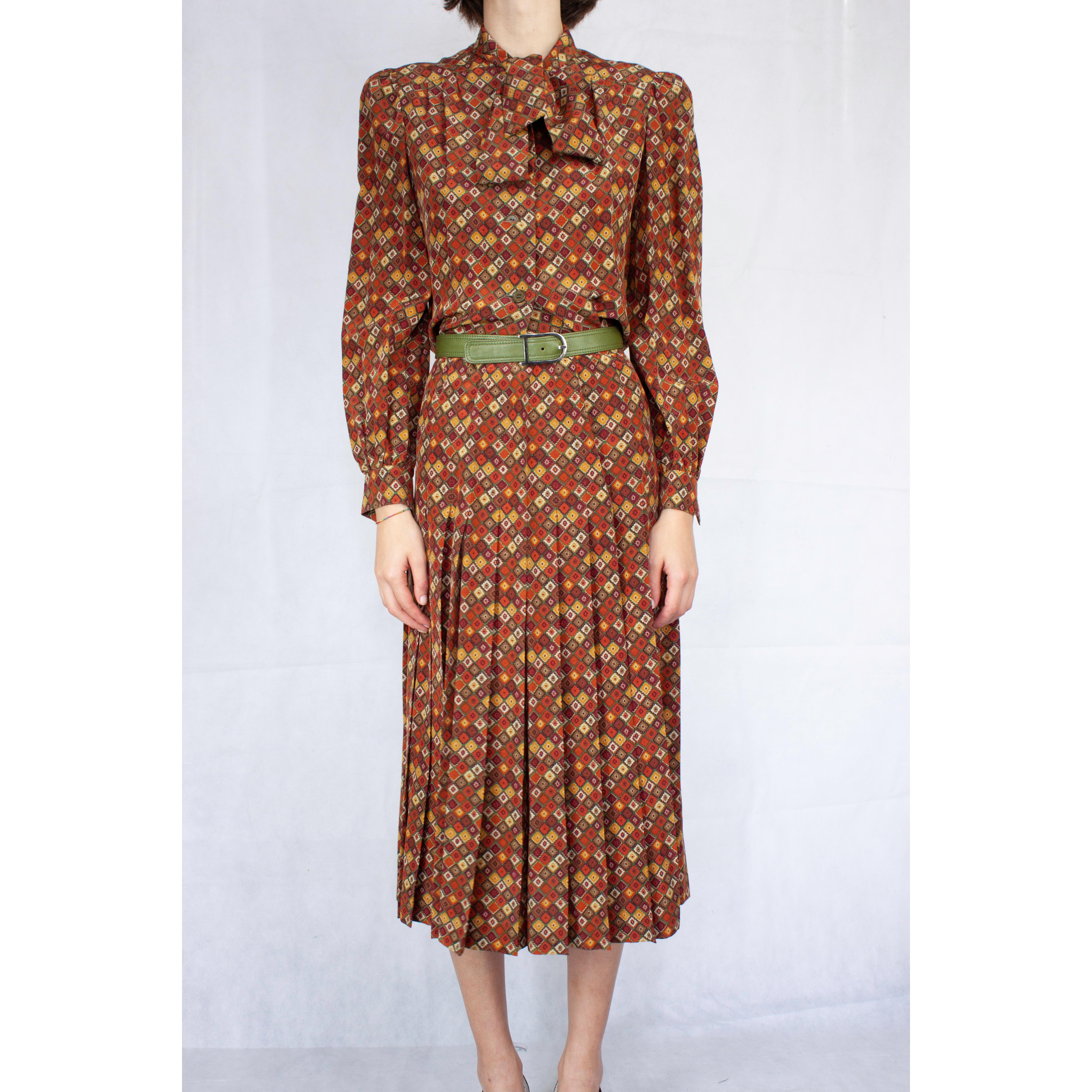 
This smart two piece daywear outfit is constructed from a lightweight silk viscose with a stylised floral print on an olive coloured background. The shirt features a neck tie collar and long slightly puffed sleeves with barrel cuffs. Bust and back