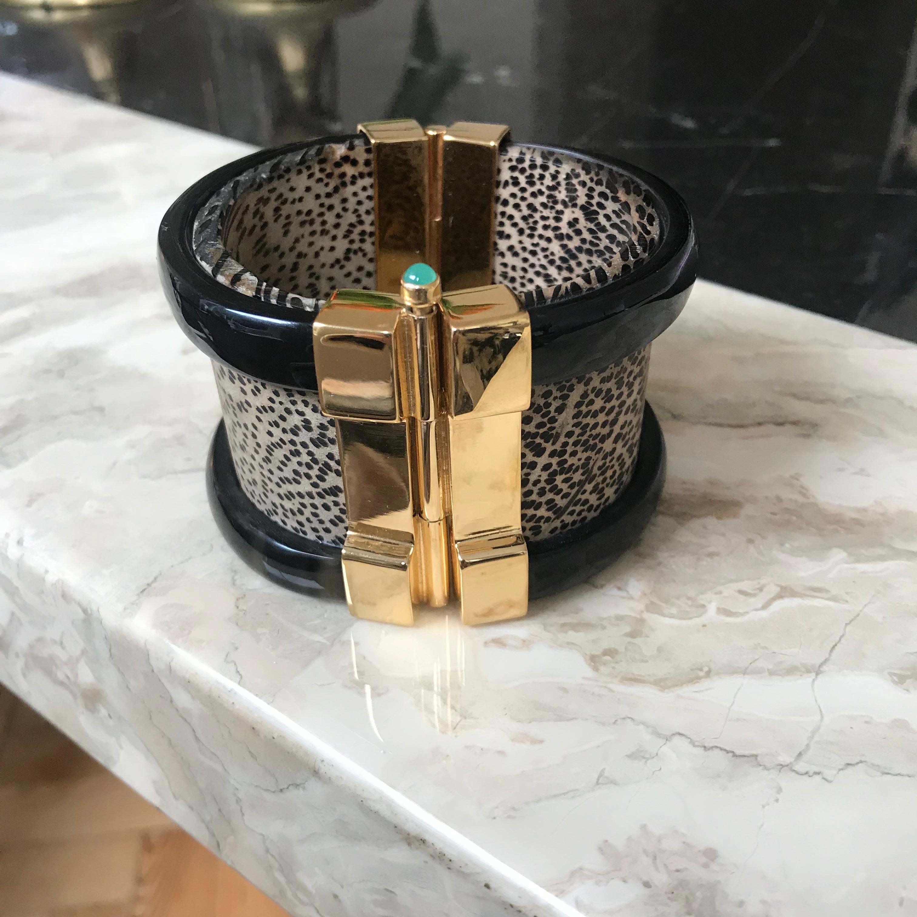 Cuff bracelet crafted from African wood and cow horn. The customizable 18k gold plated pin-clasp is set with a choice of ruby or emerald cabochon. Inspired by warrior style cuffs worn by former Vogue editor Diana Vreeland. 

Hand crafted by artisans