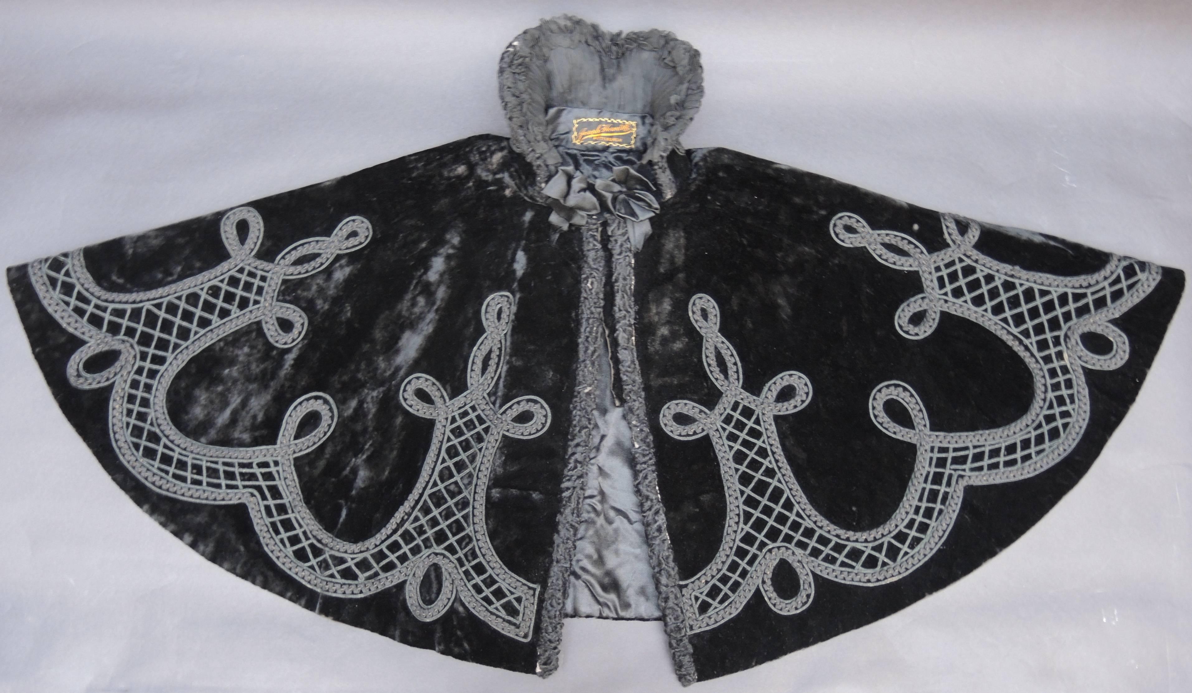 Cette cape victorienne a été fabriquée par la société Joseph Horn de Pittsburgh (Pennsylvanie) dans les années 1890. La Corde est en velours de soie agrémentée à la main de rubans et cordons de soie tressés et plissés. La fermeture avant et le col