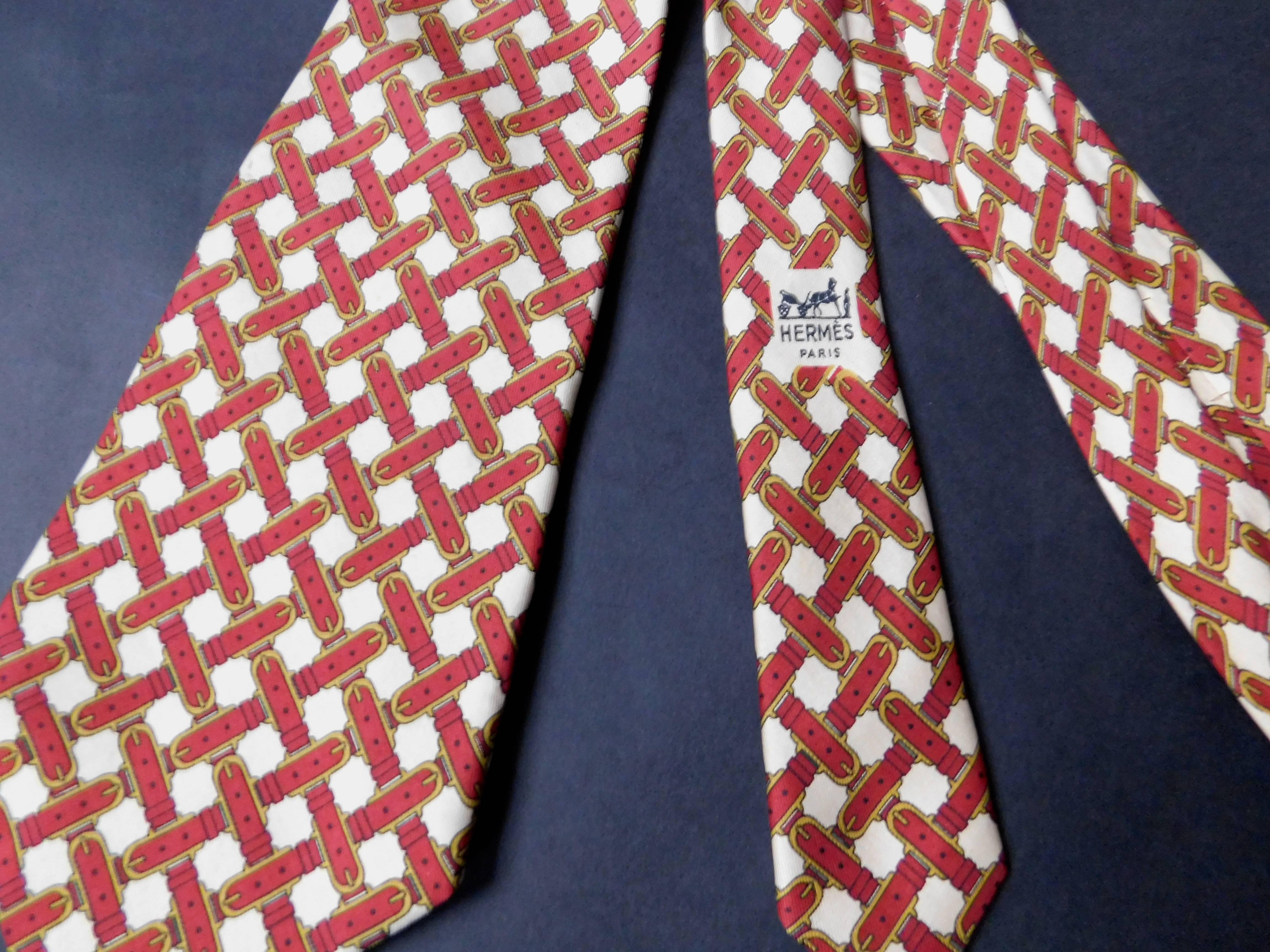 A vintage hermes mens silk tie printed overall pattern of woven stirrup buckles. Classic width and colors of cream and burgundy. Wear it as a tie or  as a sash with jeans .
The bottom width =11 cm
mid width =7cm.