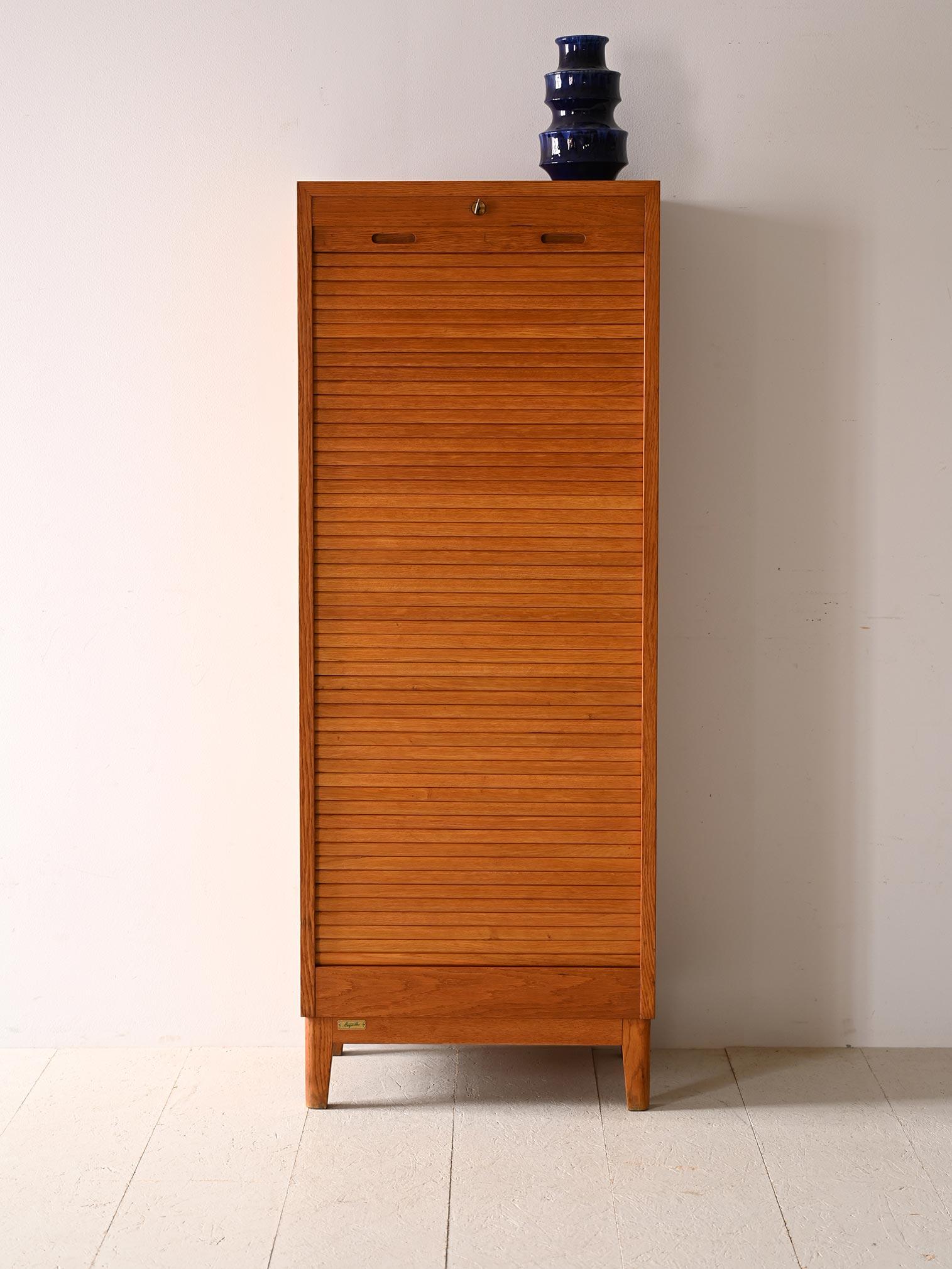 Scandinavian-made rolling shutter file cabinet.

This piece of Nordic modernism traces mid-century taste and style with clean, modern lines and refined details.
The light oak wood frame is suitable for inclusion in different types of environments