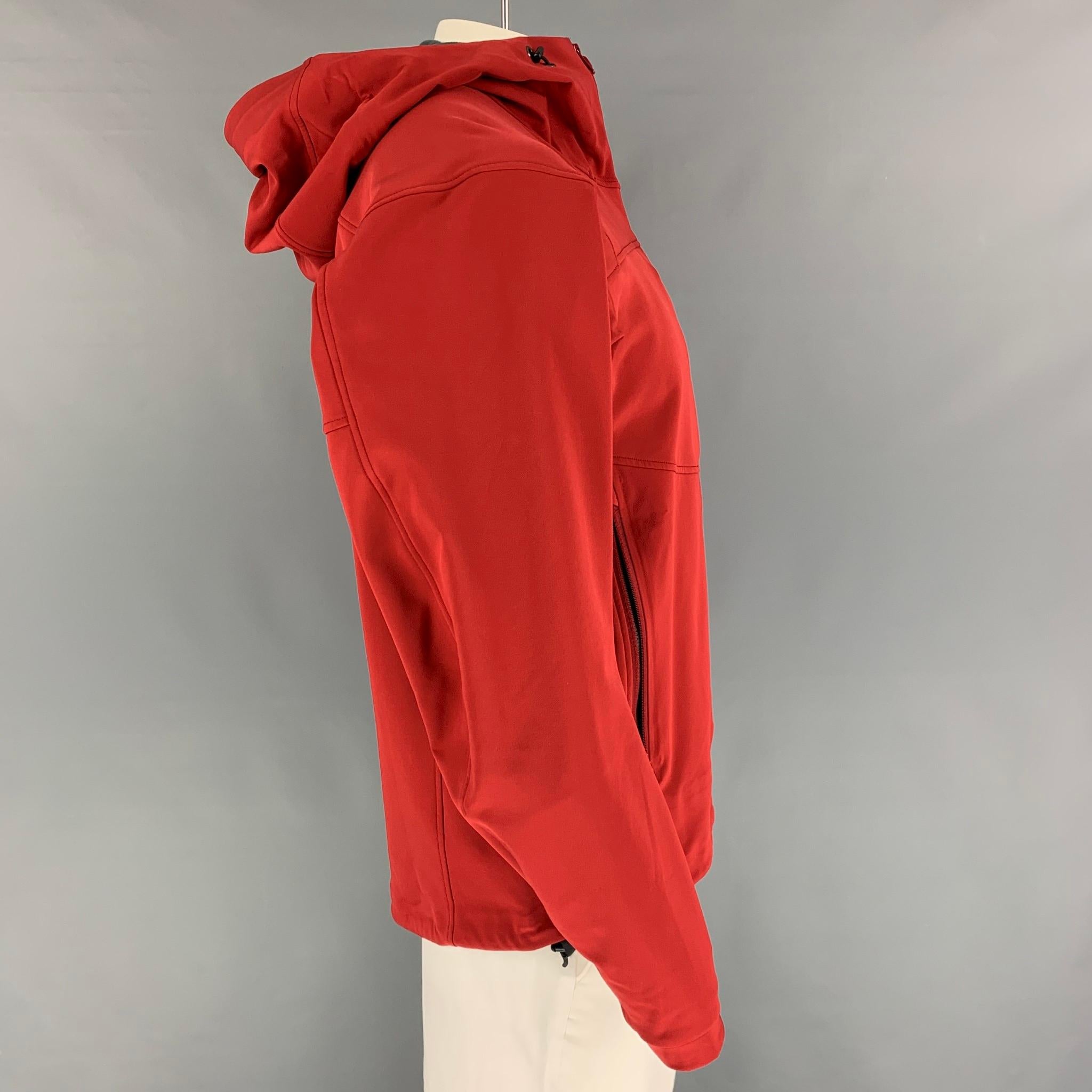 ARCTERYX jacket comes in a red nylon blend with a grey fleece liner featuring a hooded style, front pockets, sleeve pocket, and a full zip up closure. 

Very Good Pre-Owned Condition.
Marked: L
Original Retail Price: