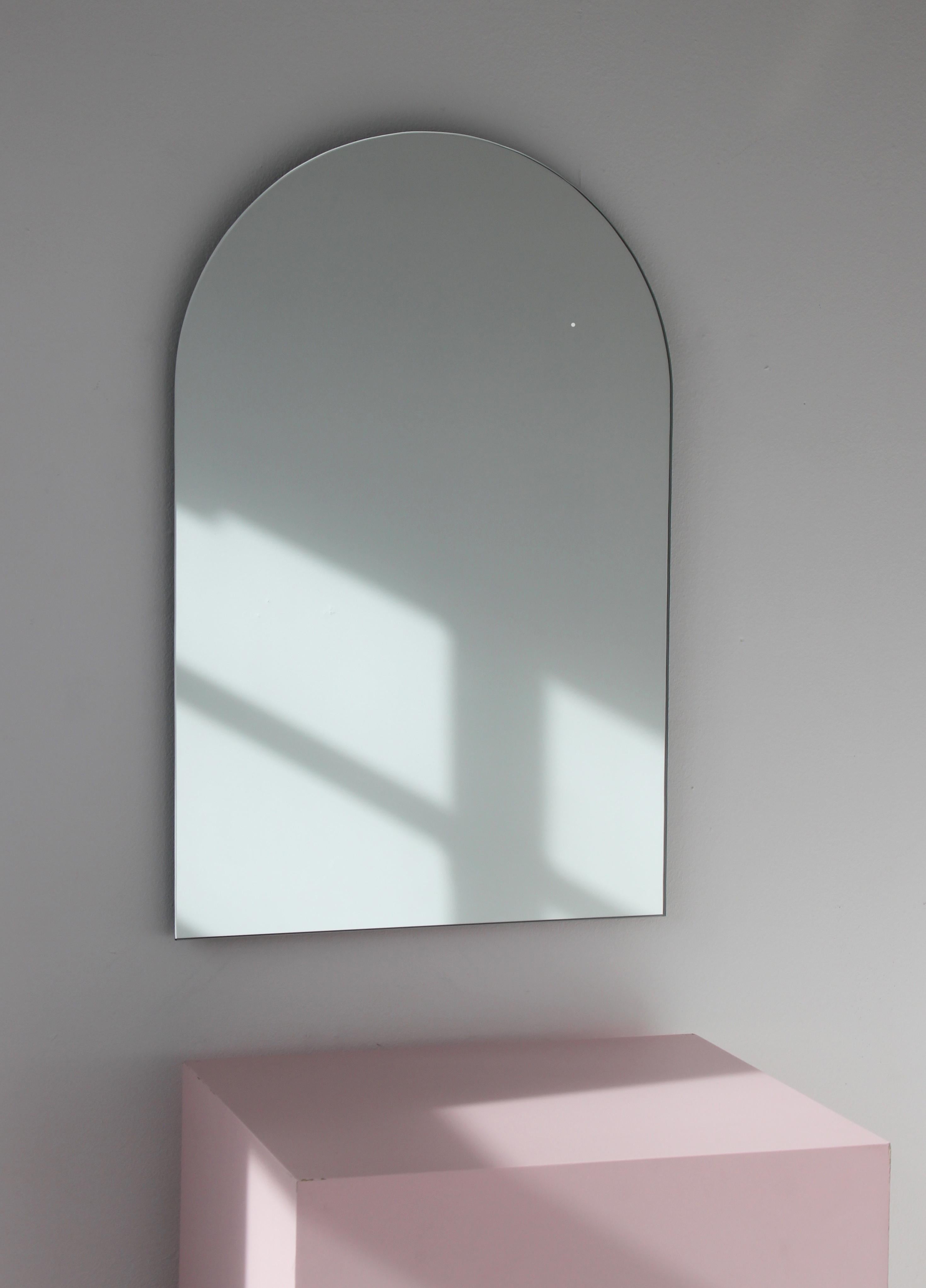 Minimalistischer gewölbter rahmenloser Spiegel. Hochwertiges Design, das dafür sorgt, dass der Spiegel perfekt parallel zur Wand steht. Entworfen und hergestellt in London, UK.

Ausgestattet mit professionellen Platten, die im eingebauten Zustand