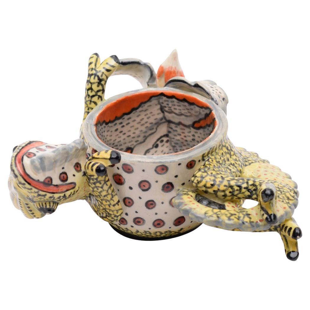 Delight in the whimsical charm of the Chameleon Egg Cup, a masterpiece from Ardmore Ceramics. Hand-sculpted by Nkwenke Scholar and adorned with vibrant hues by Thandeka Shabalala, this piece stands 2 inches high and measures 4 inches in both length