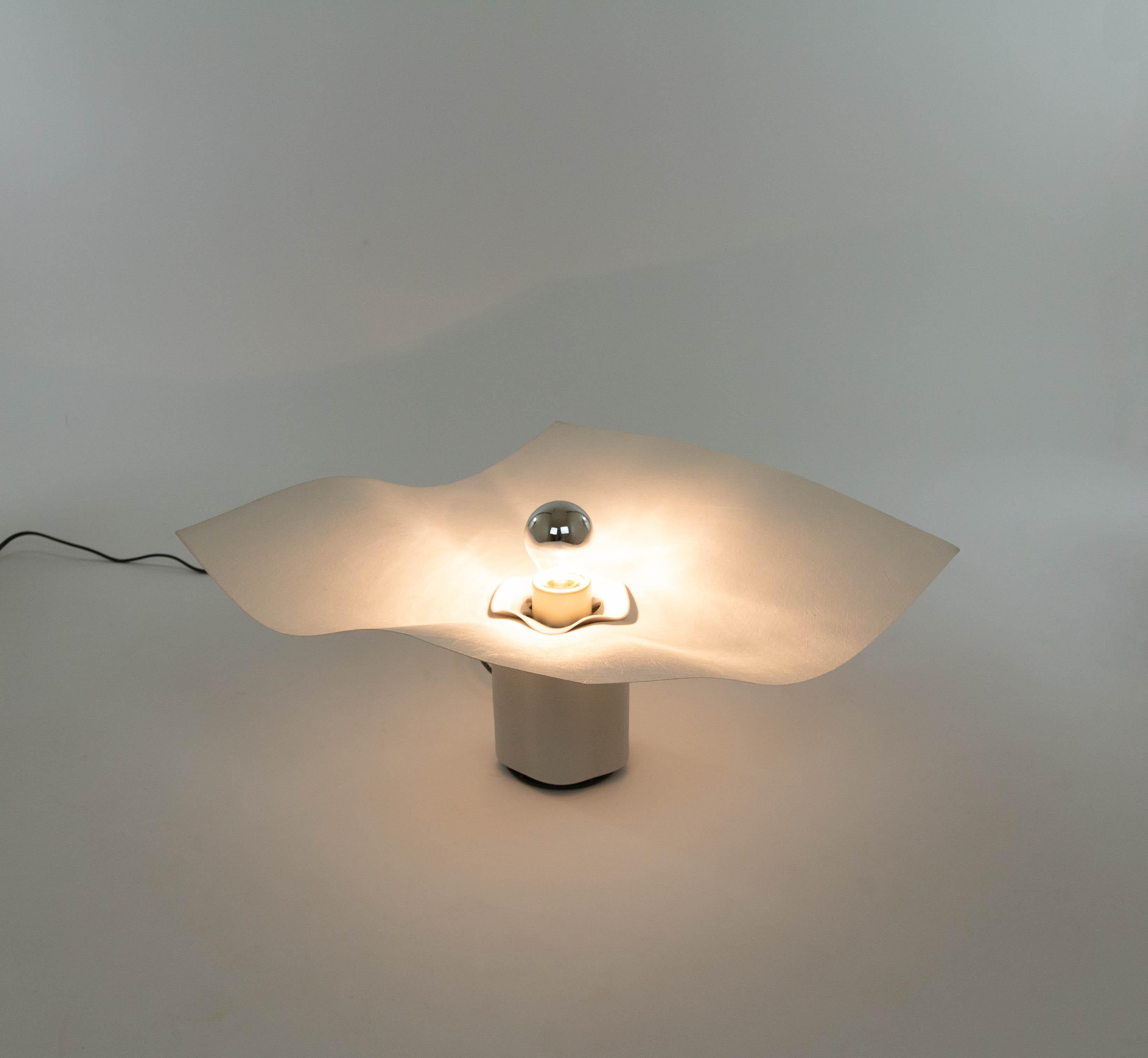 Lampe de table Area 50, conçue par Mario Bellini et fabriquée par Artemide dans les années 1970.

La lampe se compose d'une base en porcelaine blanche mate (18 cm de haut) et d'un diffuseur couleur crème en textile synthétique. Une pièce en
