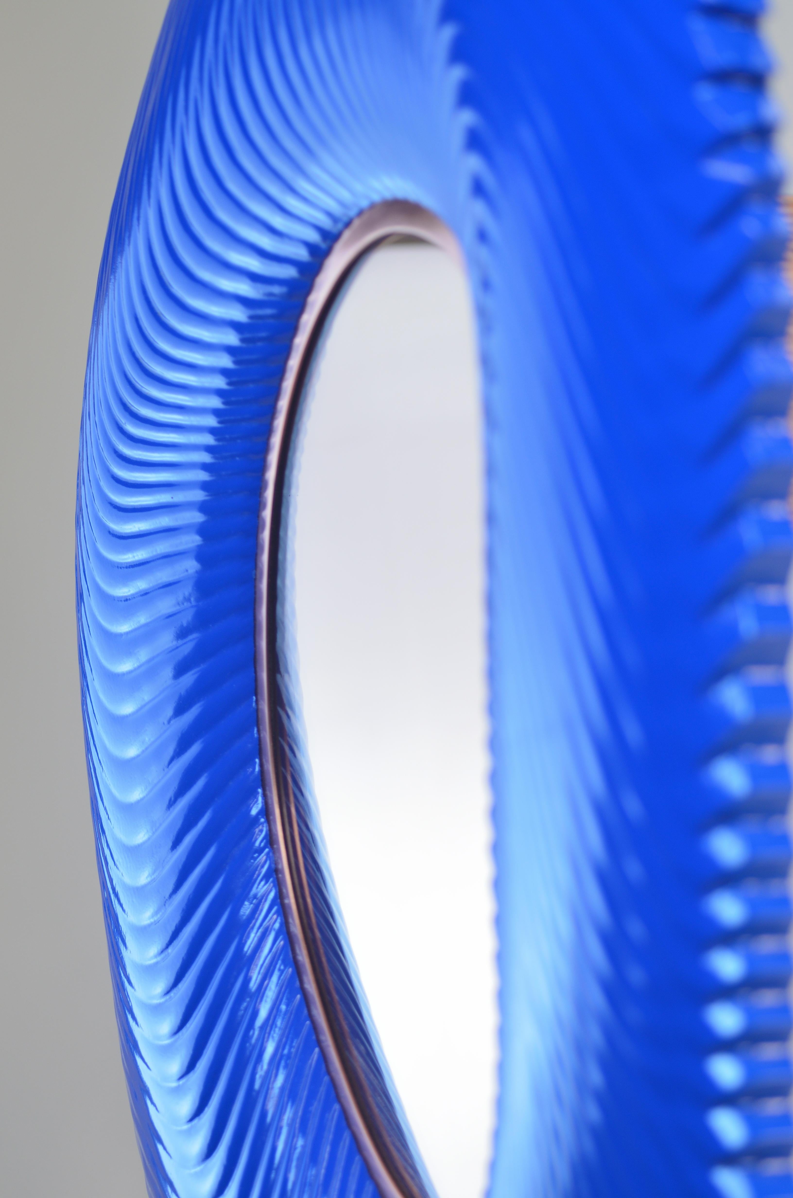 Le miroir tendu Ares bleu lapis en vernis satiné avec miroir pêche présente une magnifique laque bleu lapis sur un cadre surréaliste usiné en 3D. Le miroir pêche est contrebalancé par une garniture en cuivre, qui se marie harmonieusement avec la
