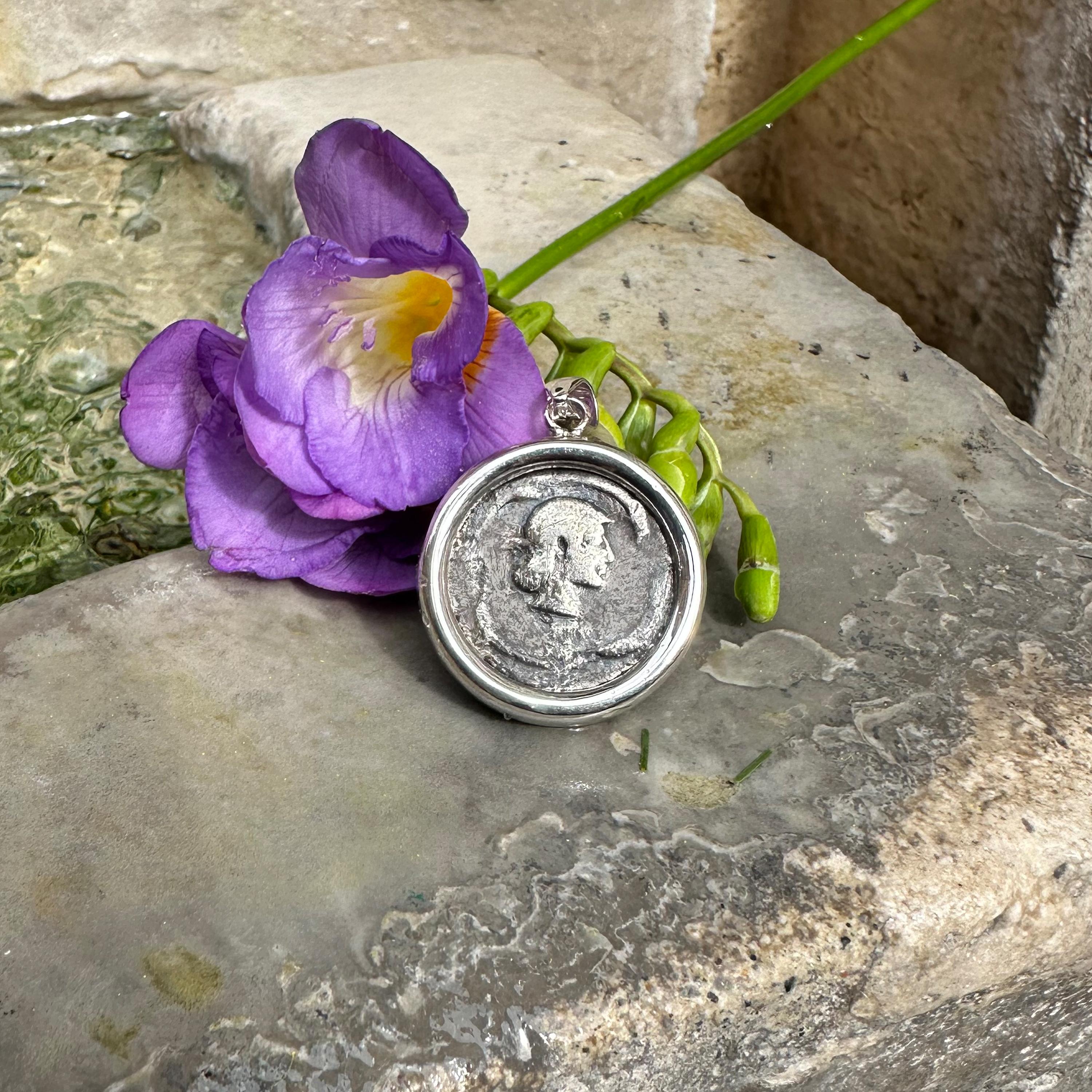 Discover an authentic ancient Greek coin pendant featuring a stunning depiction of Aretusa’s head on the front, surrounded by four playful dolphins. 

Aretusa, a revered nymph in Greek mythology, is famously known for her transformation. Pursued by