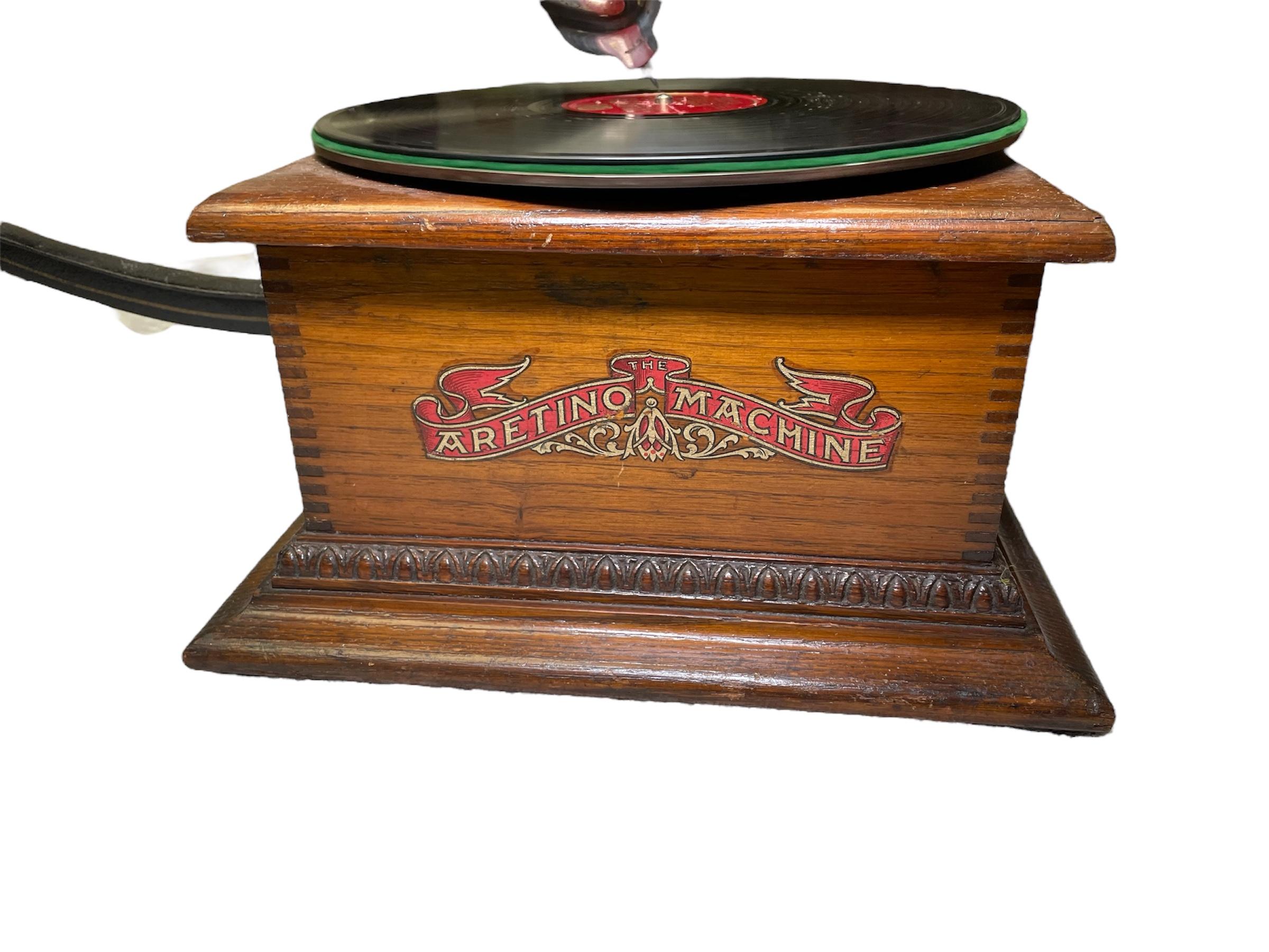 Il s'agit d'un phonographe machine Aretino. Elle représente un meuble en bois de forme carrée, surmonté d'un plateau rond où l'on place un disque/enregistrement que l'on peut entendre lorsque l'aiguille fixée à la corne à pédale en forme de fleur à