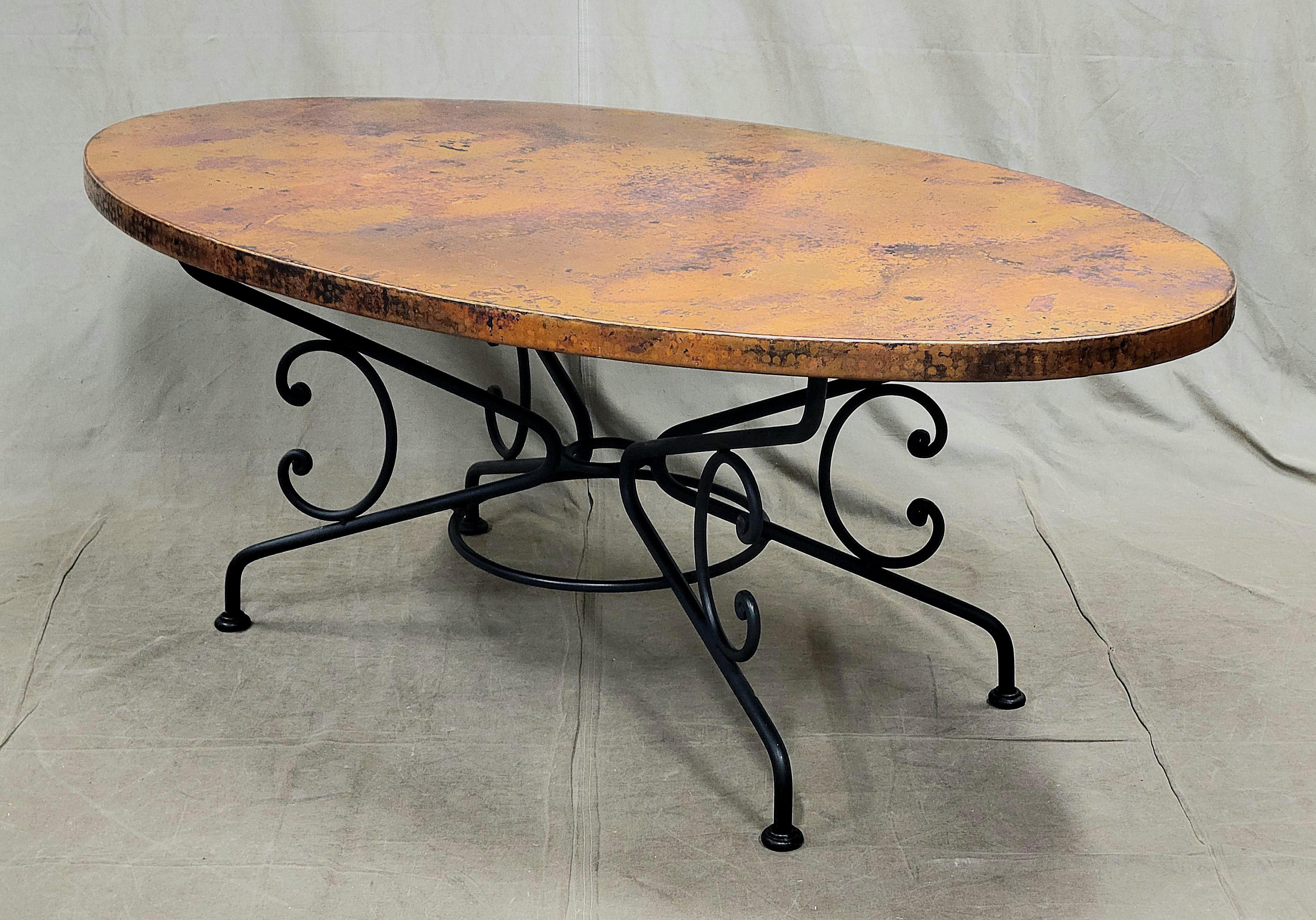 A gorgeous Arhaus hammered and patinated copper top and iron arabesque base oval dining table. A stunning centerpiece of a rustic dining room or kitchen. The surface is sealed with a lacquer so simply wipe down with a damp rag for easy clean up.