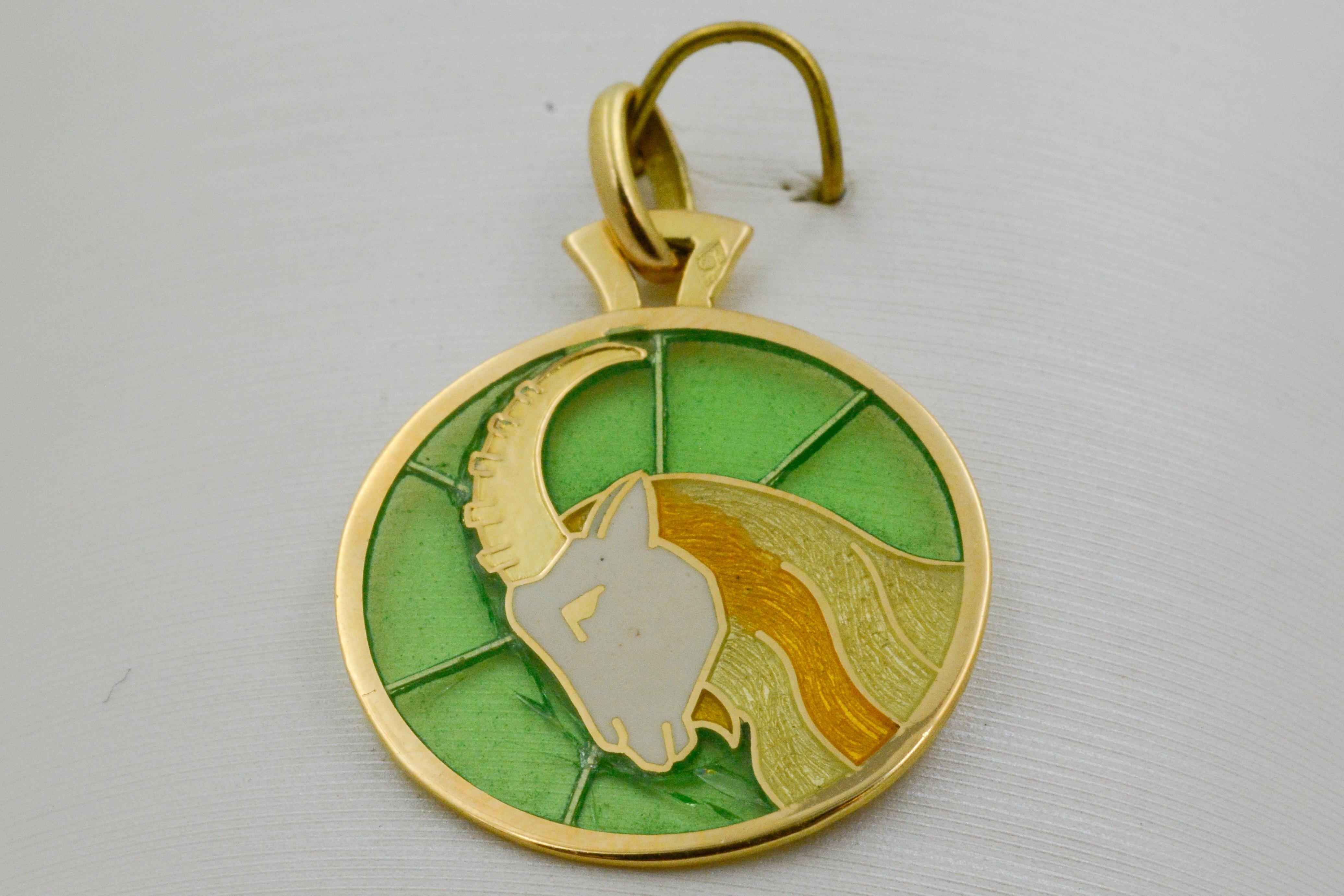 This Plique a Jour pendant features the Capricorn zodiac sign as the central design. The goat is crafted in hand enameled yellow glass on a green background with 18 karat yellow gold outlines and border. 
