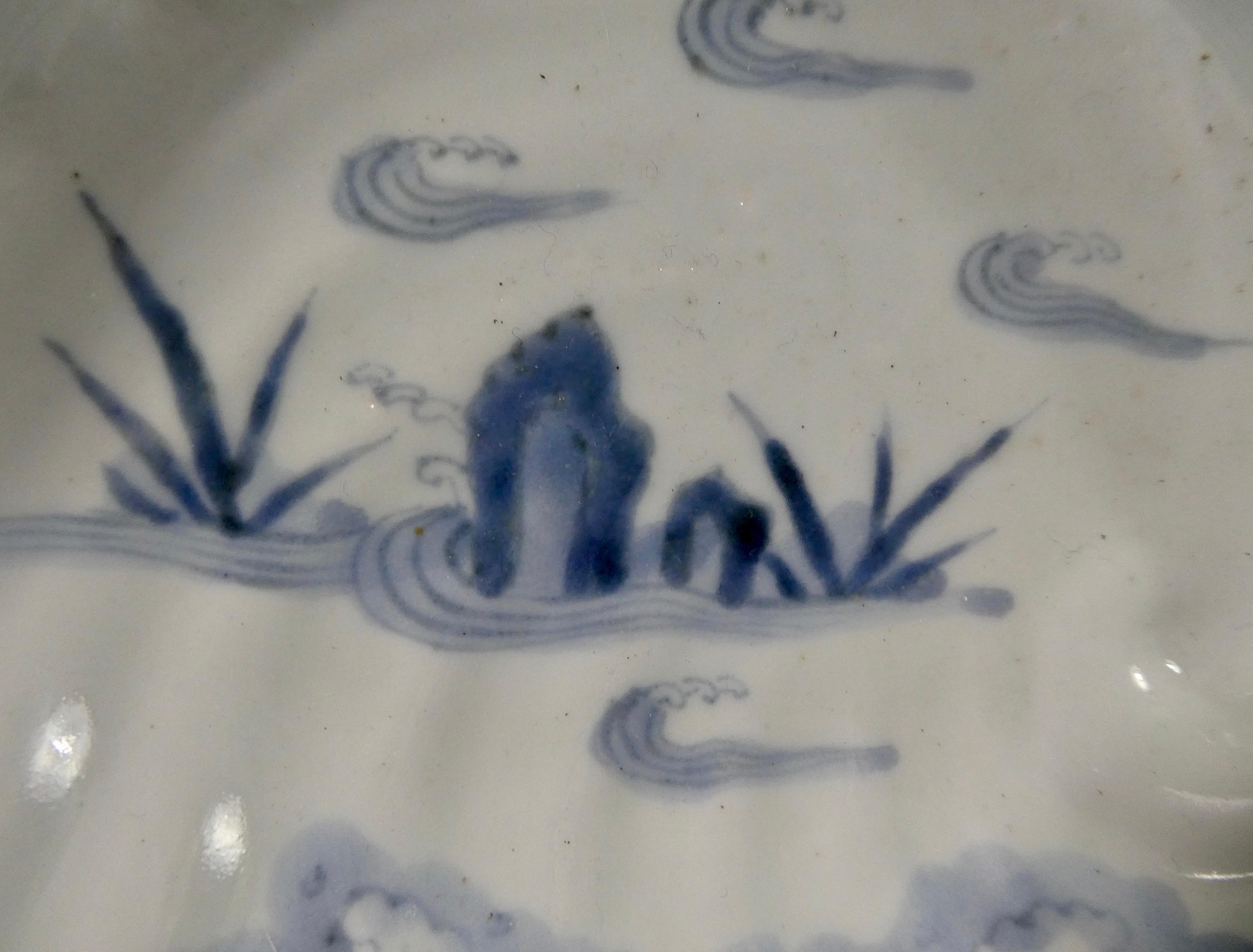 A Japanese porcelain dish, Arita, circa 1720, Edo Period. The dish moulded in the shape of an abalone or awabe shell. Painted in underglaze blue, with a scene of rocks and plants in a river, amongst stylised waves. The reverse with further water