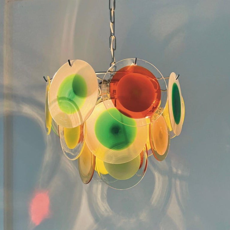 Gino Vistosi late 60's hanging lamp, 18 round handmade Murano glass discs (colored, milky and transparent) hang in a circle on a chromed frame on three different levels.

The cascade shape is very modern again.
 