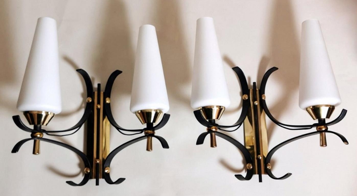 Elegant and graceful pair of wall sconces; the original and solid structure is made of brushed and polished brass; some parts have been baked in black creating a pleasant contrast; the design is sinuous but functional; the balanced arrangement of