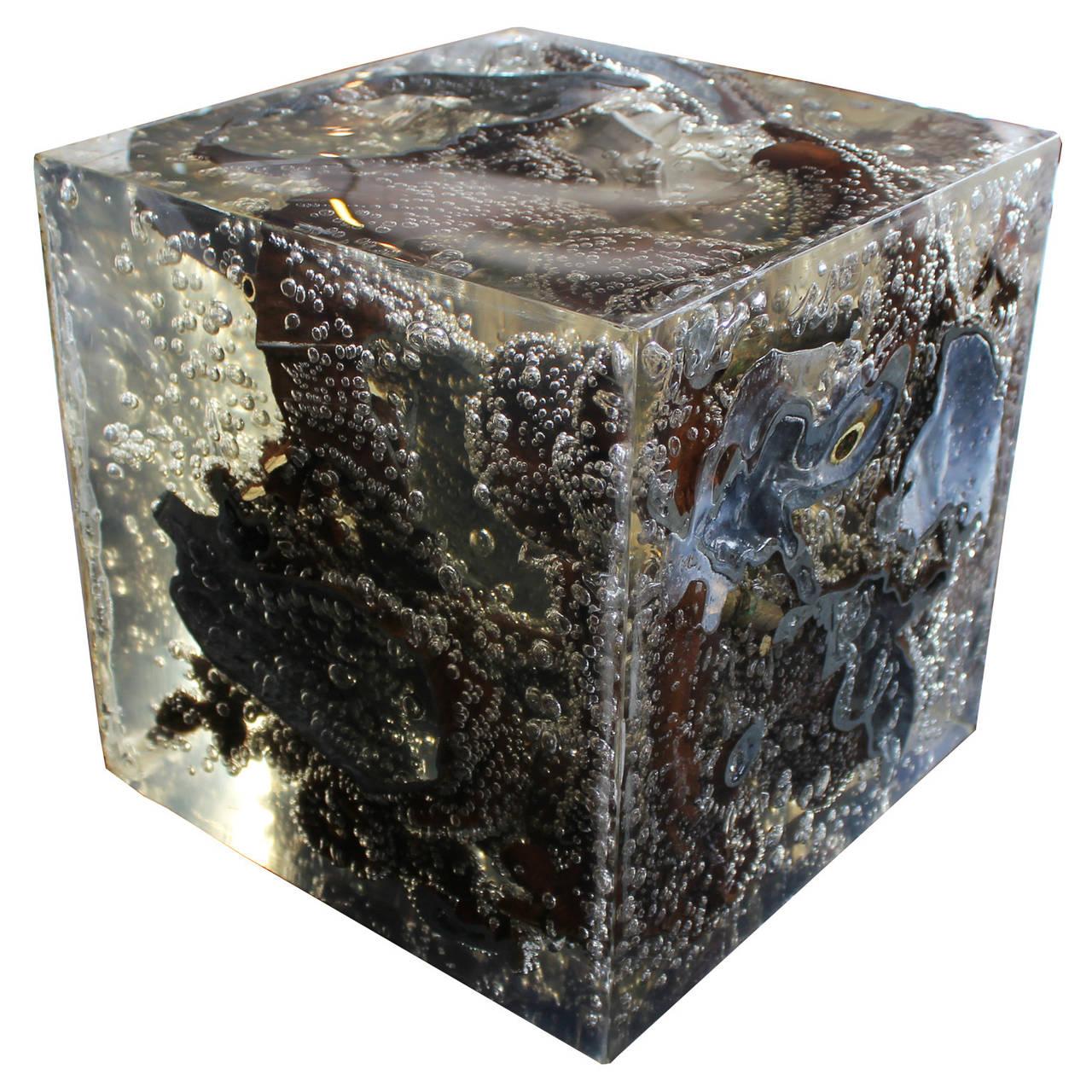 Unique modern resin sculpture with a cut pieces of bronze suspended in the resin. Within the cube are bubbles of air that create a galaxy like effect that add to the unique quality of the piece. On one of the faces of the cube is the artist's