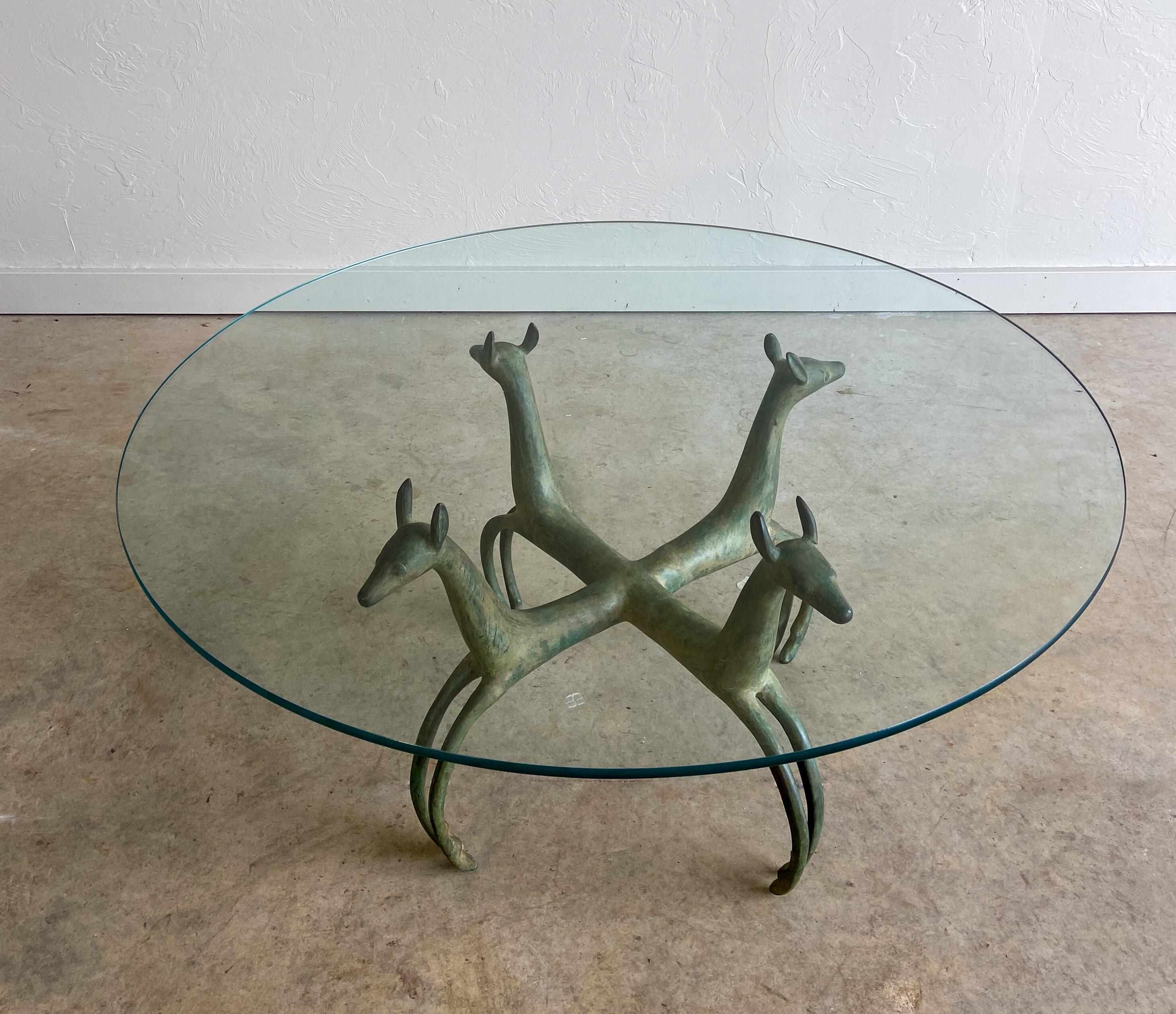 A sculptural, patinated cocktail table in the style of Armand-Albert Rateau. The base is made up of four stylized cast bronze deer supporting a round glass top. Will ship without glass top.
