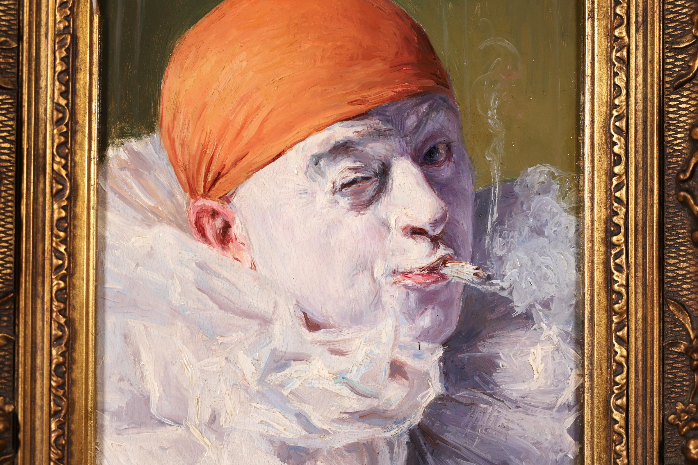 A delightful oil on panel circa 1900 by French impressionist painter Armand Francois Henrion depicting a portrait of a Pierrot - a French clown - wearing white ruffles and an orange hat and smoking a cigarette. The portrait is set against an olive