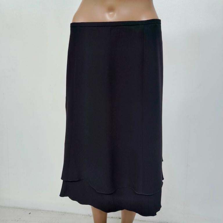 This Armani Collezioni layered midi skirt is a beautifully balanced exercise in understated Italian elegance. Cut from refined black stretch crêpe, it falls straight over the hips before opening into two soft, scalloped tiers that ripple gently with
