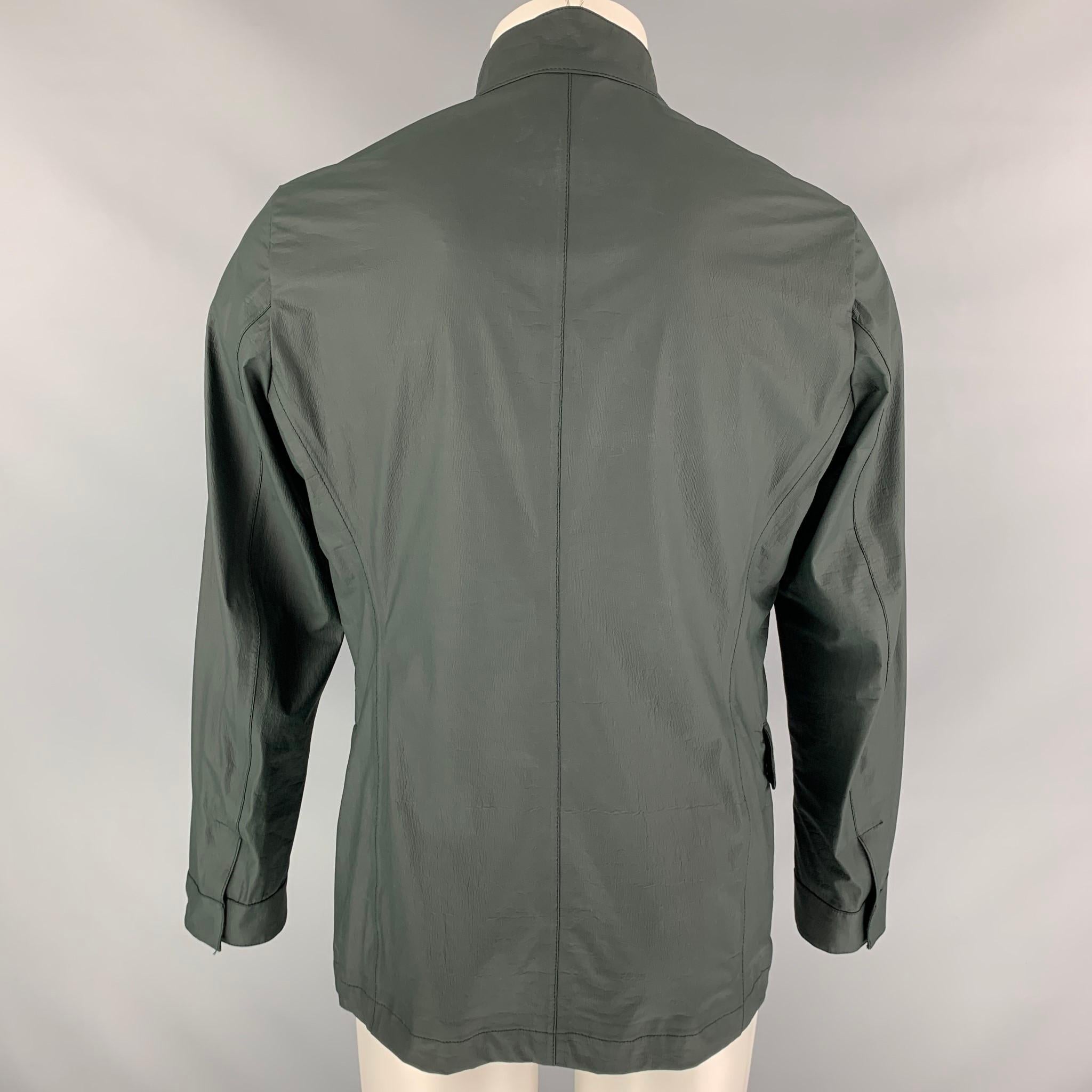 La giacca ARMANI COLLEZIONI è di colore verde scuro in polietilene con materiale idrorepellente, collo alto, quattro tasche frontali e chiusura con zip. 

Nuovo con etichetta. 
Contrassegnato: 48

Misure:

Spalla: 17.5 pollici.
Petto: 38