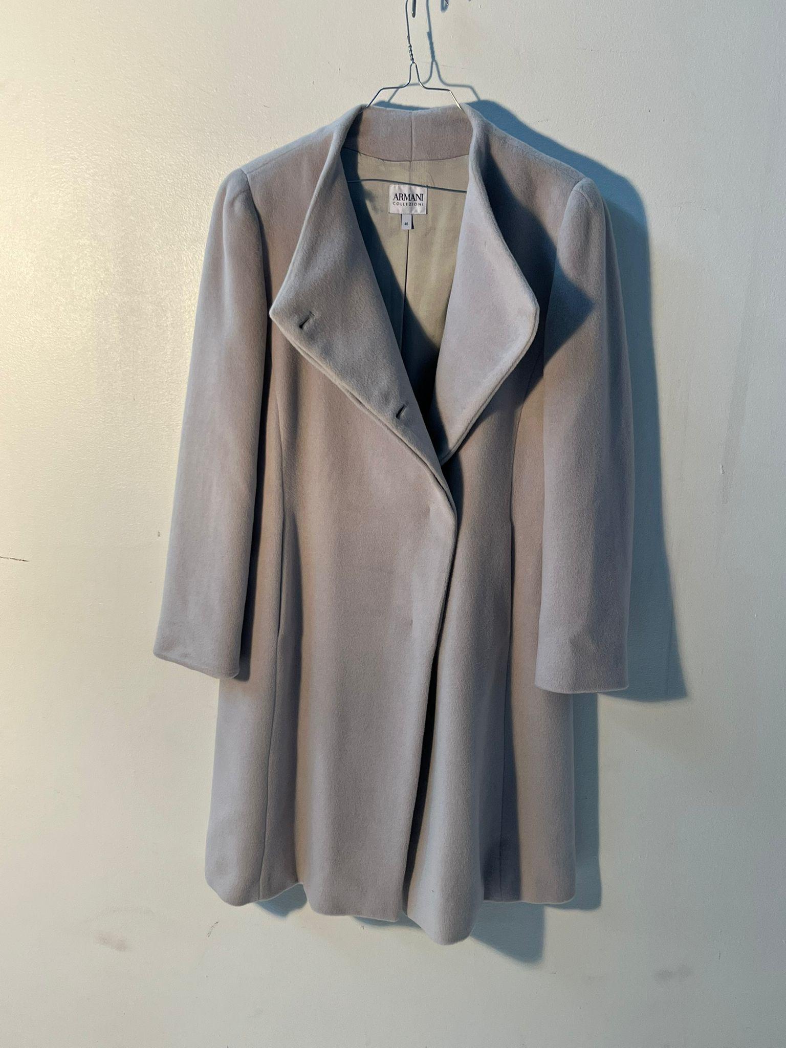 This elegant Armani Collezioni coat is crafted from a luxurious wool–cashmere blend, offering a soft, smooth texture with a refined drape. Presented in a sophisticated light grey tone, the coat features a clean, minimalist silhouette typical of