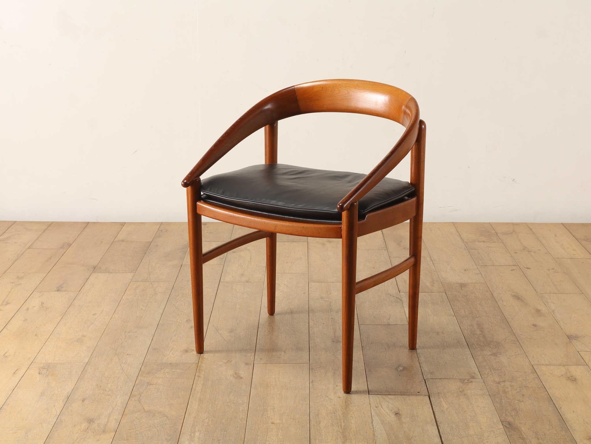 This armchair, crafted in Denmark and estimated to be from the 1970s, features a distinctive curved silhouette that flows gracefully from the backrest to the tips of the armrests. The beautifully grained teak wood frame not only offers reliable