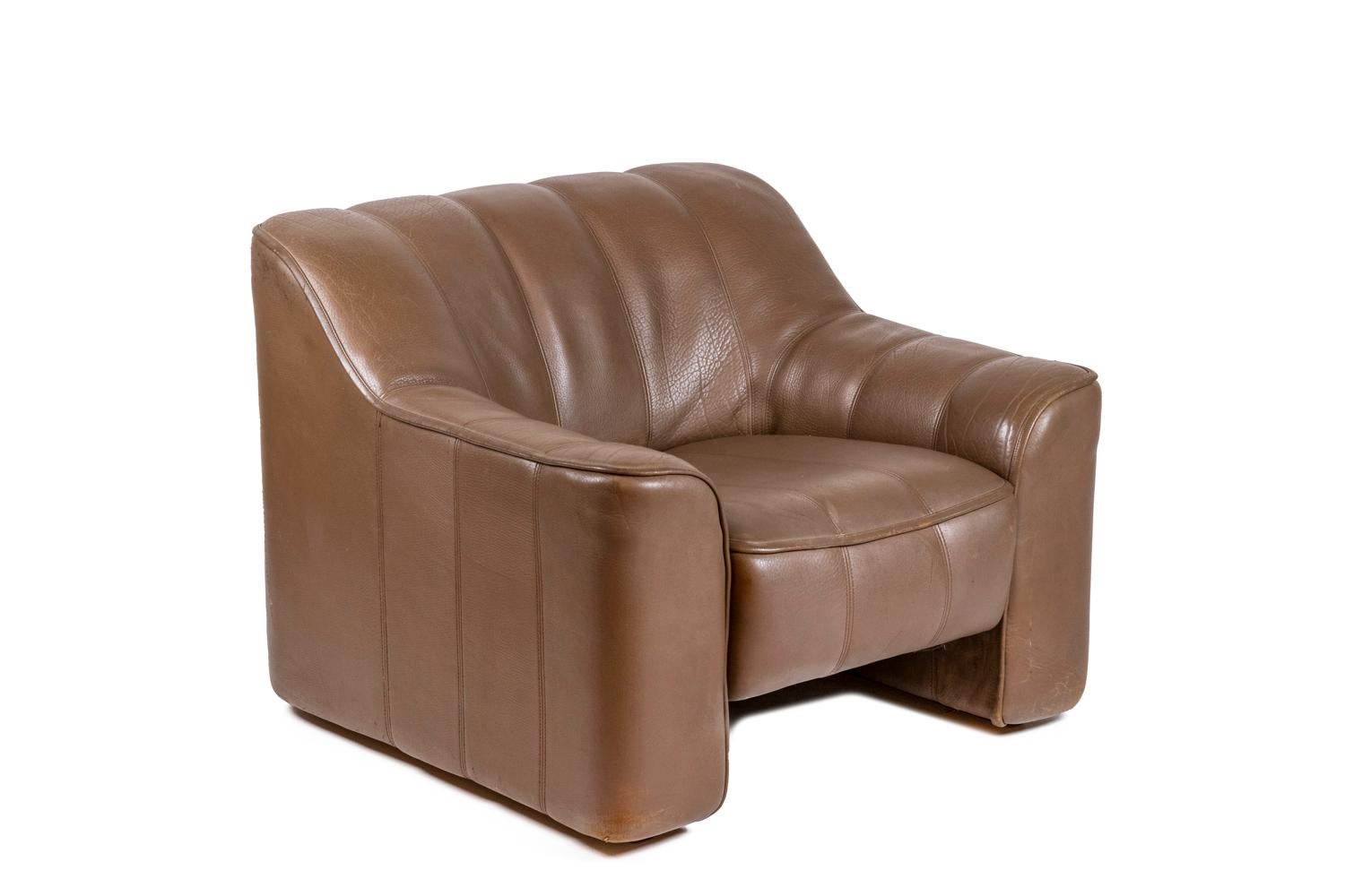 Armchair and ottoman in grooved leather, glossy brown color. Large armchair with its sliding seat. Square or cube shaped ottoman.

Work realized in the 1970s.

Dimensions : armchair : H 70 x W 86 x D 80 cm ; ottoman : H 35 x W 60 x D 55 cm.