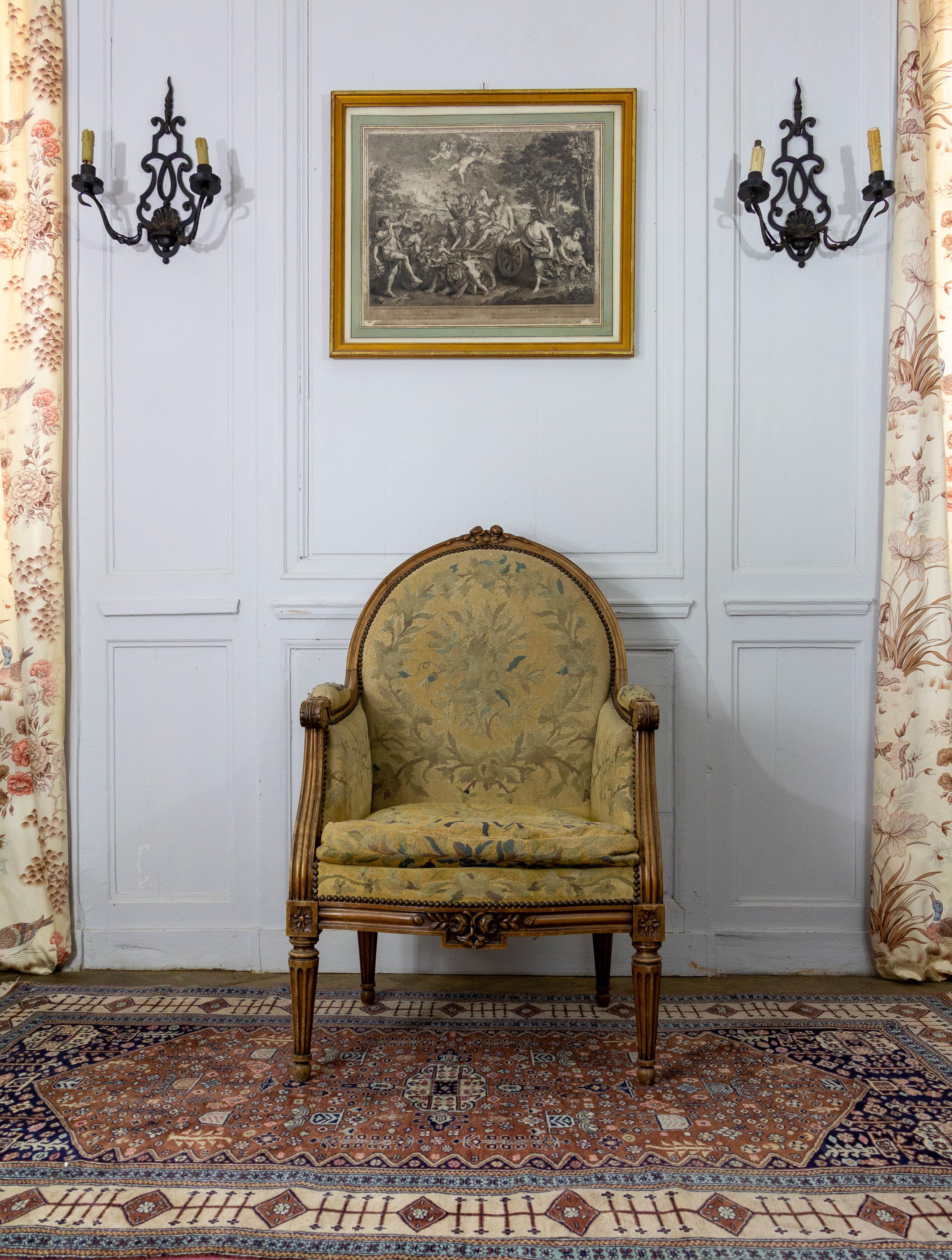 Very beautiful armchair bergère of Louis 16 style from the middle of the 19th century. The wood is richly carved with flowers and foliage and the feet are fluted. Beautiful tapestry in blue and green tones, on the back a beautiful crown of flowers