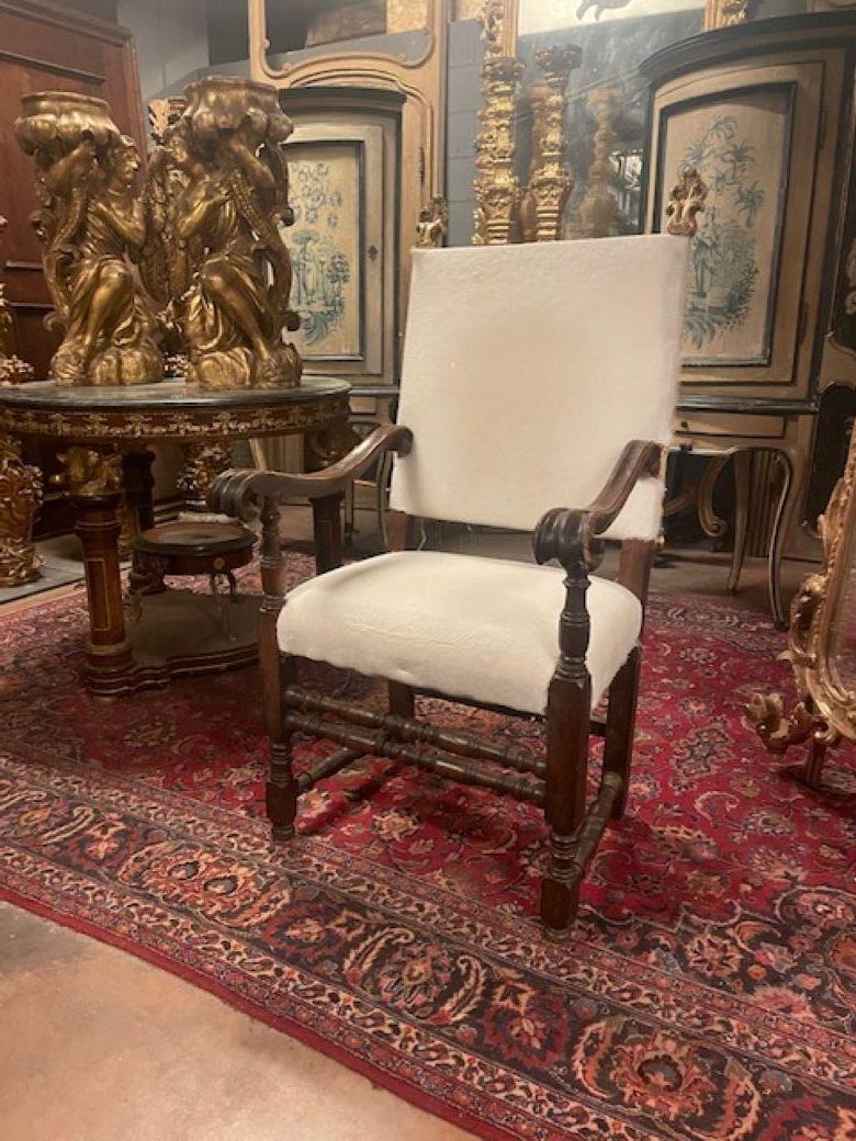 Sillón muy antiguo, silla alta a la cabecera de la mesa en preciosa madera de nogal tallada a mano, reposabrazos rizados tallados y patas de carrete torneadas, con particulares detalles de hojas doradas en la parte superior del respaldo, respaldo y