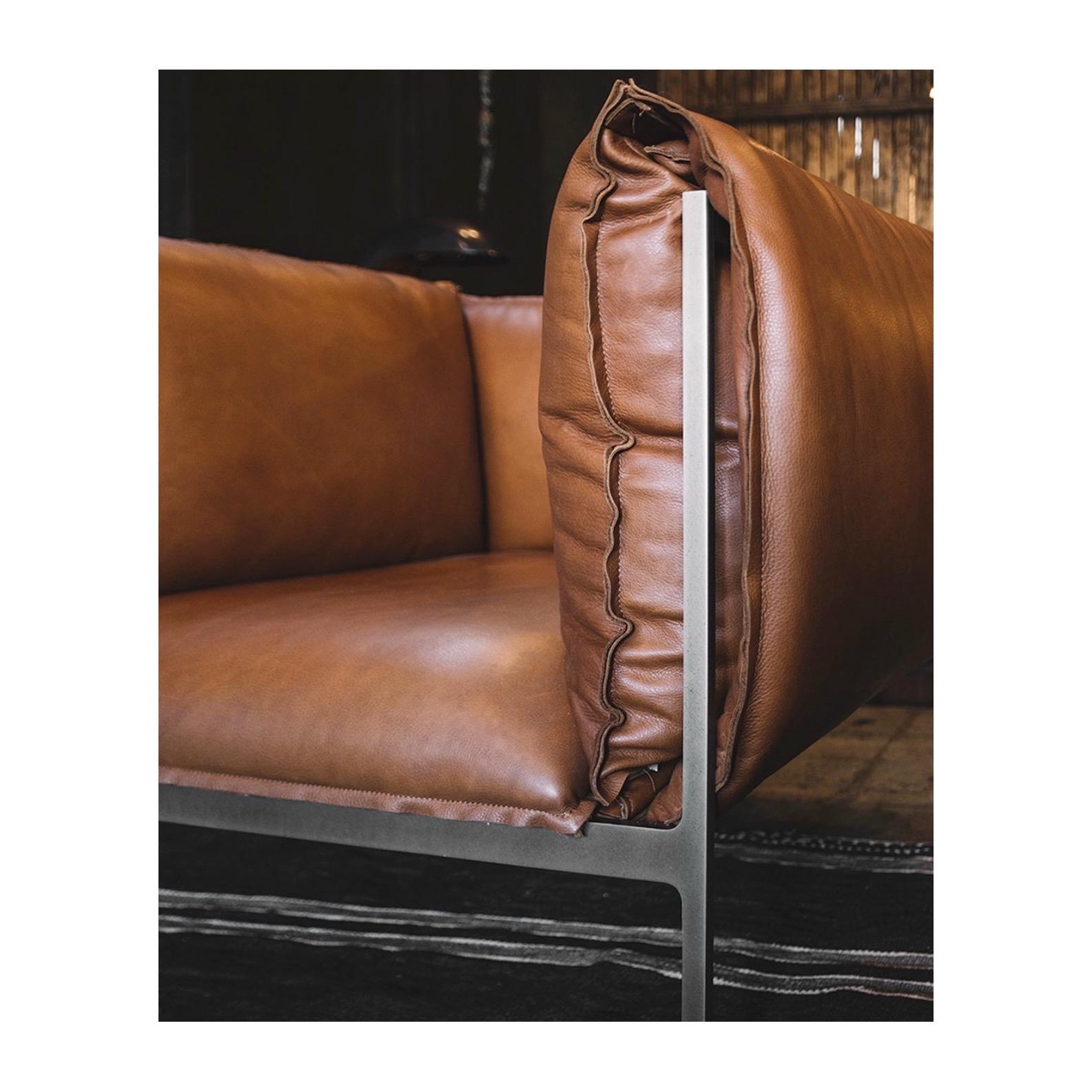 Bulging over its edges, this contemporary single sofa seat by Klein Agency screams comfort. Puffy cushions hug the laser cut steel frame, creating a supple cocoon, demanding you to wallow in its softness. With its bulky front and bulging back, the