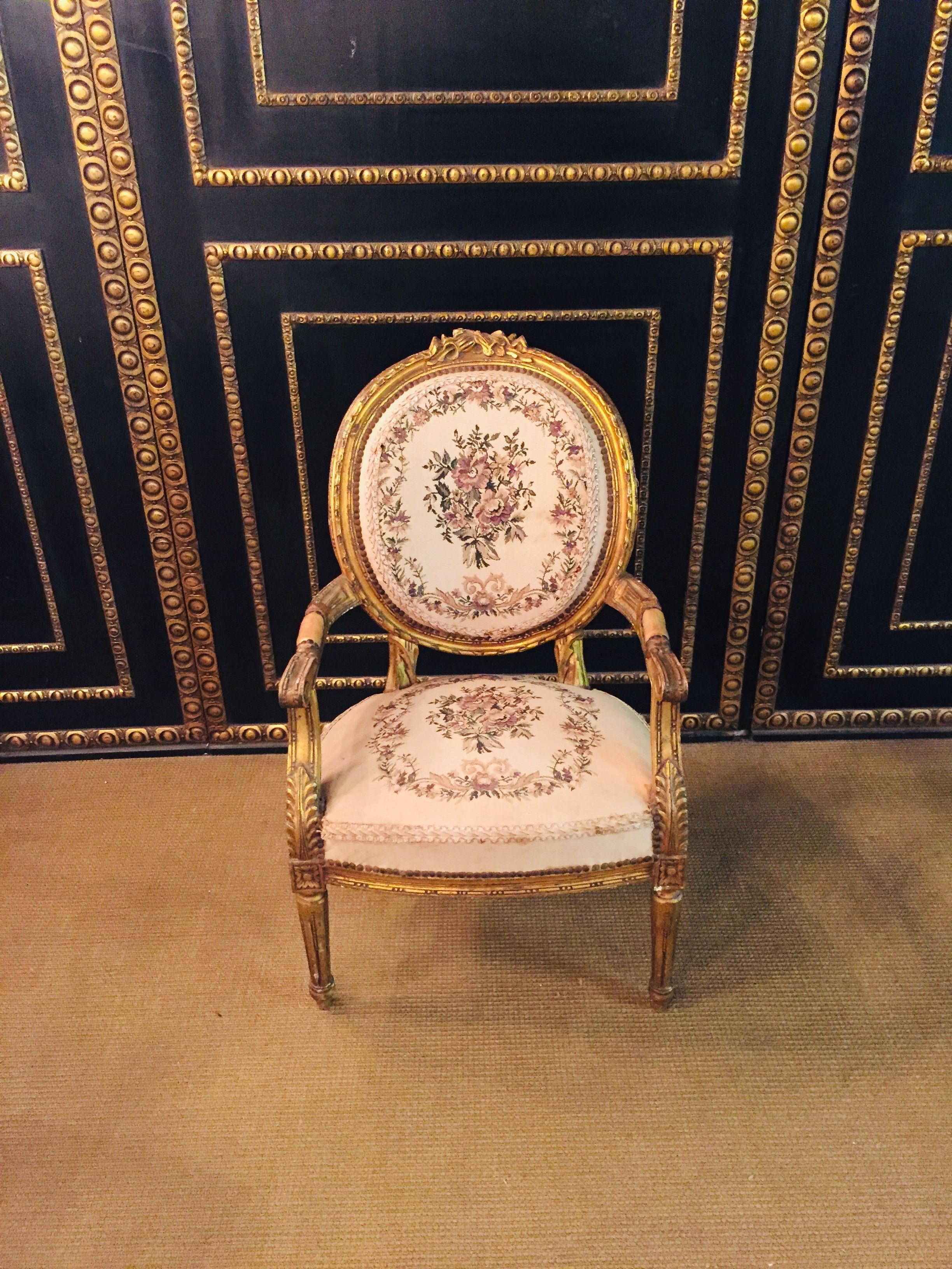 Solid beechwood, set and gilded. Cambered and carved frame on fluted, pointed legs. Curly armrests. Straight supports with applied acanthus leaves. Rising armrests in oval back frame ending in carved Rocaillenbekrönung. Seat and backrest are