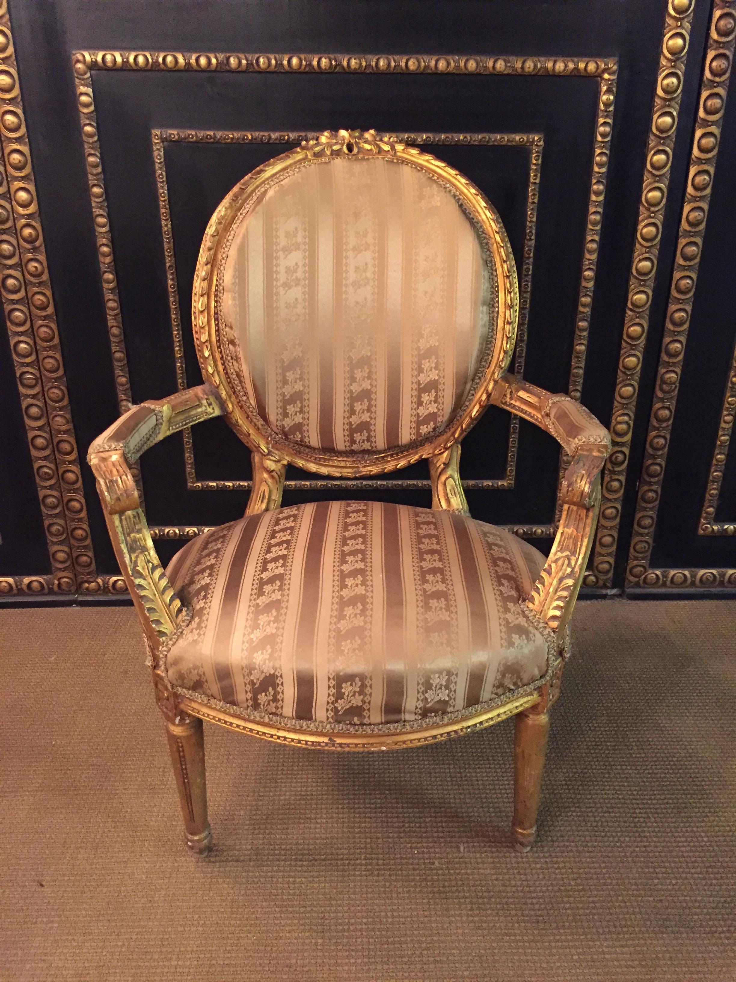 Solid beech wood, set and gilded. Cambered and carved frame on fluted, pointed legs. Curly armrests. Straight supports with applied acanthus leaves. Rising armrests in oval back frame ending in carved Rocaillenbekrönung. Seat and backrest are