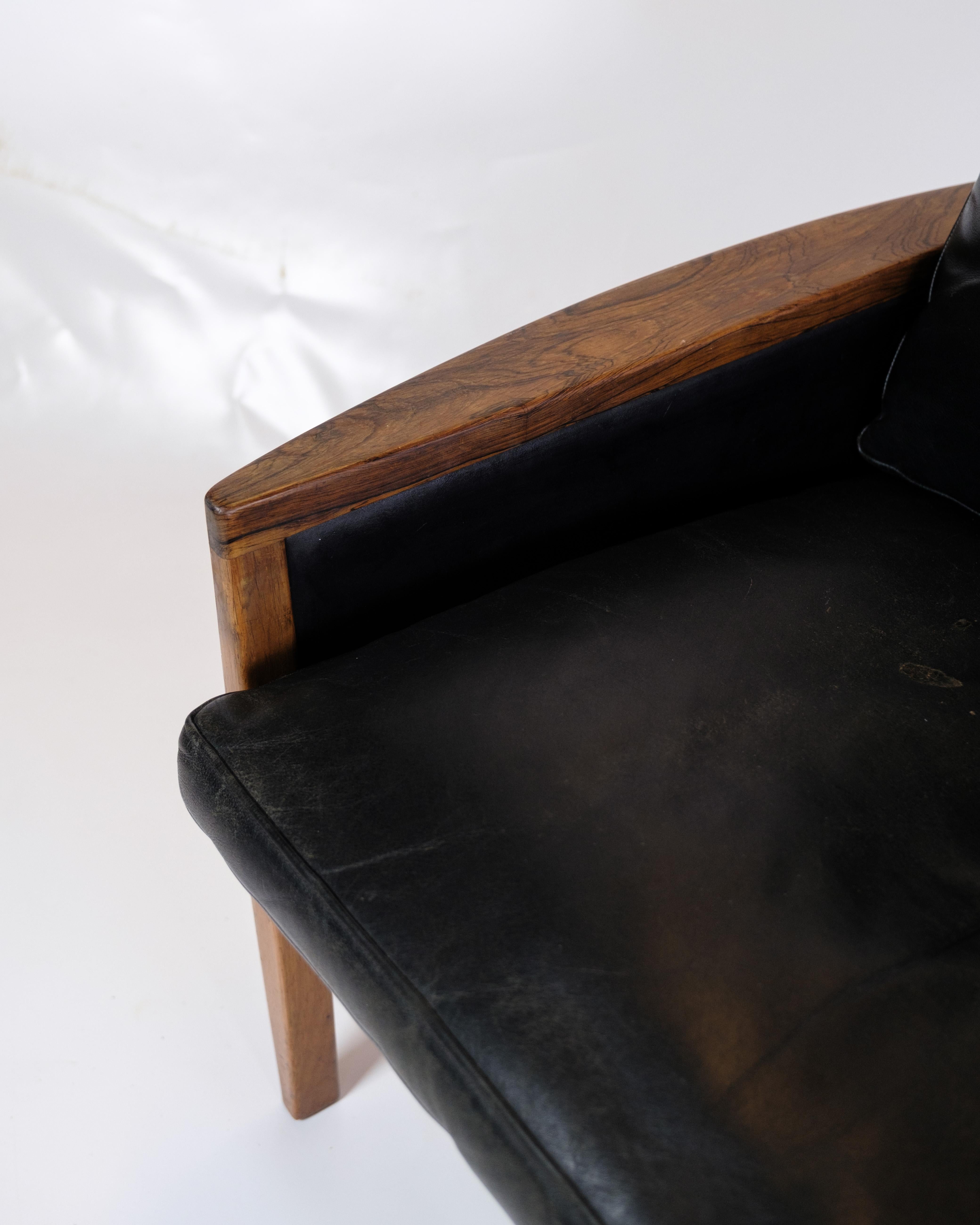 Cet élégant fauteuil en bois de rose avec coussins en cuir noir est un splendide exemple de design danois classique. Le bois de rose, avec sa couleur profonde et son grain fin, confère à la chaise un aspect unique et luxueux, tandis que le cuir noir