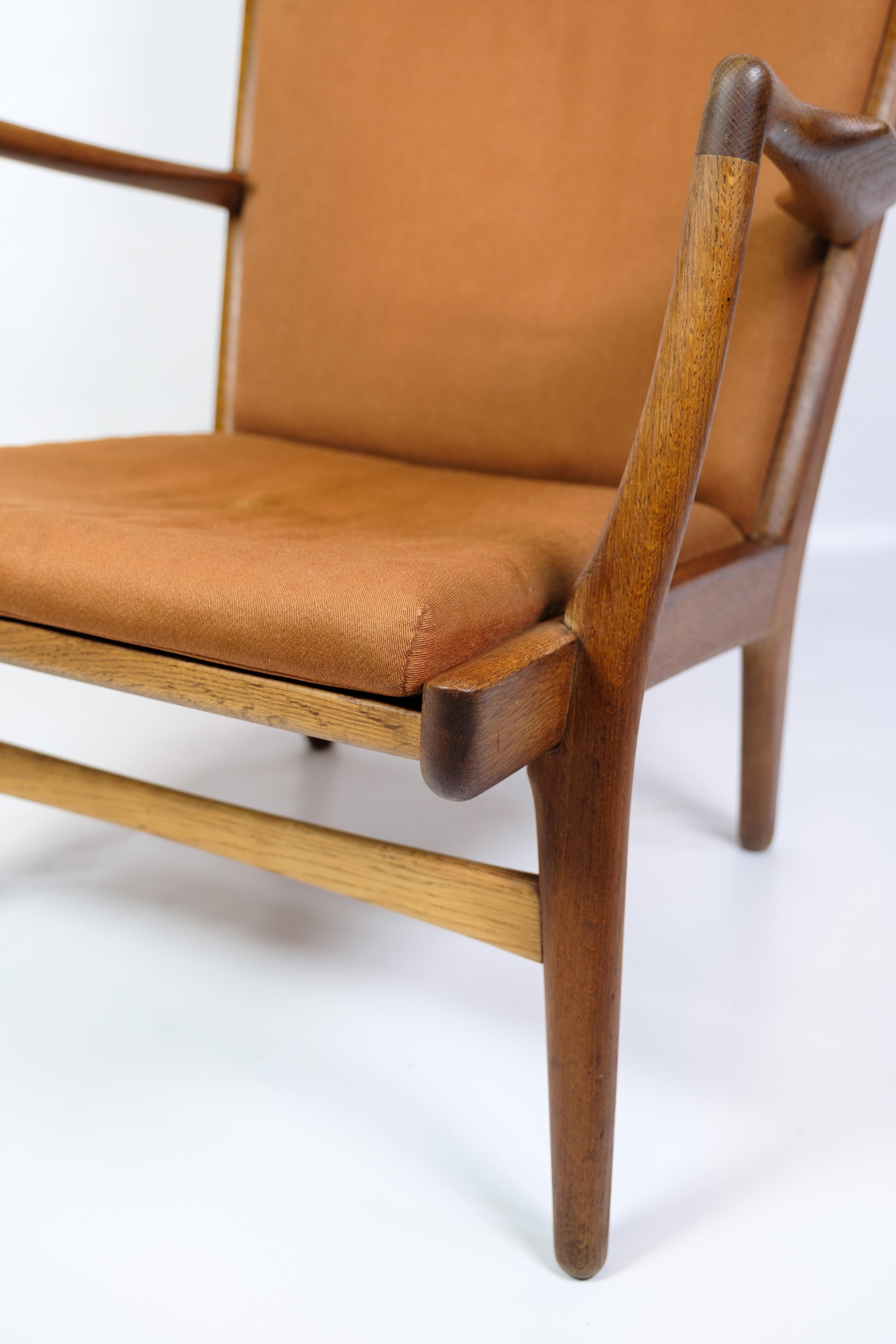 Le fauteuil AP 15, conçu par Hans J. Wegner et produit par AP Stolen en 1951, est fabriqué en chêne et revêtu de tissu orange. La chaise est connue pour son dossier haut et ses accoudoirs incurvés, qui assurent à la fois le confort et une expression