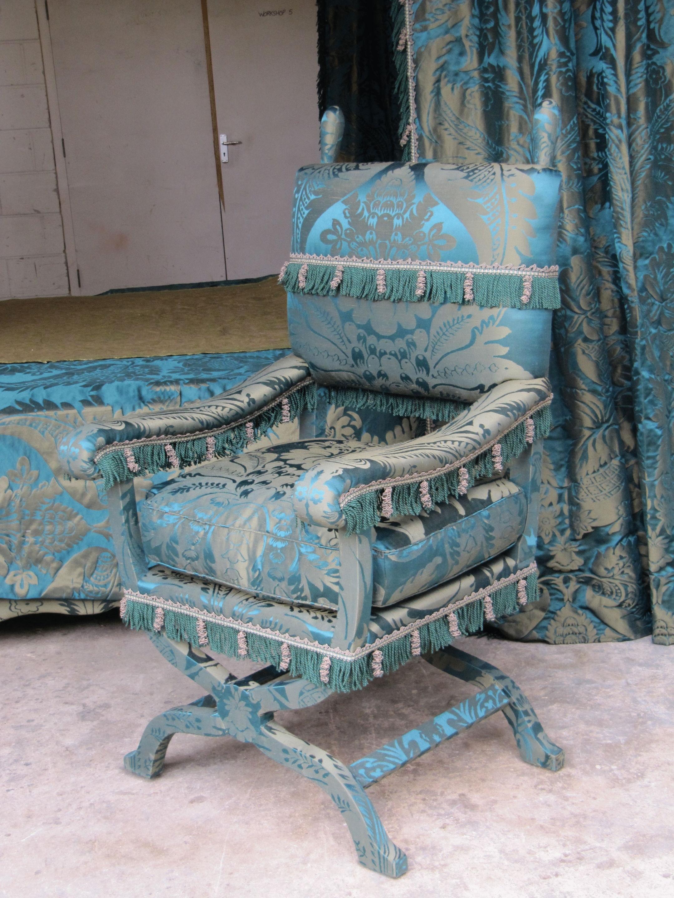 Surmounted with finials above the rectangular back and seat with a loose cushion. The scroll arms are supported by an ‘X’ frame with stretchers. 
 
Back height including finials 123 cm., 48 ½ in., seat height 55 cm., 21 ½ in.,
Width 66 cm., 26 in,