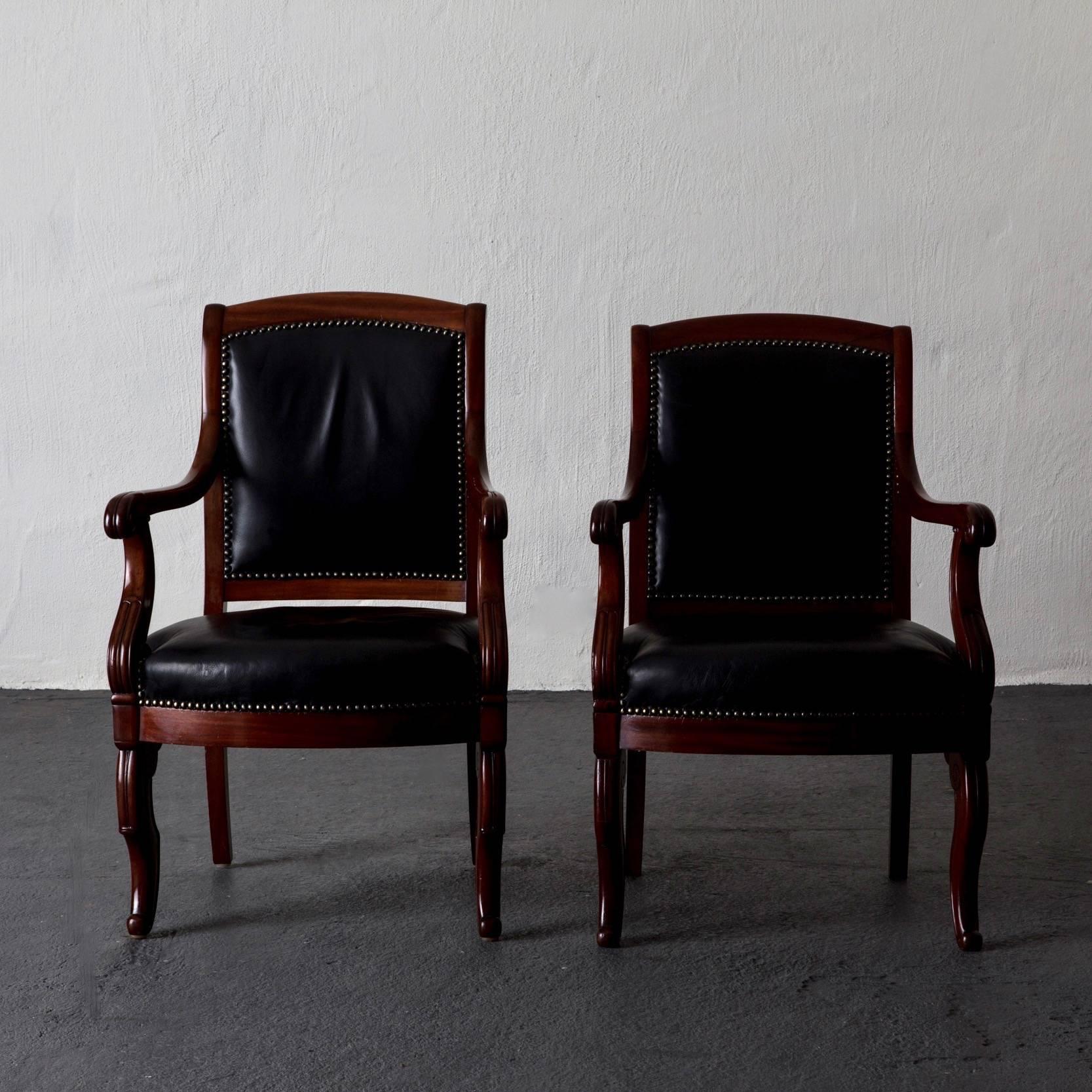 An assembled pair of French Empire armchairs made in mahogany and upholstered in a soft black leather decorated with nailheads. The chairs both comfortable and stylish.
