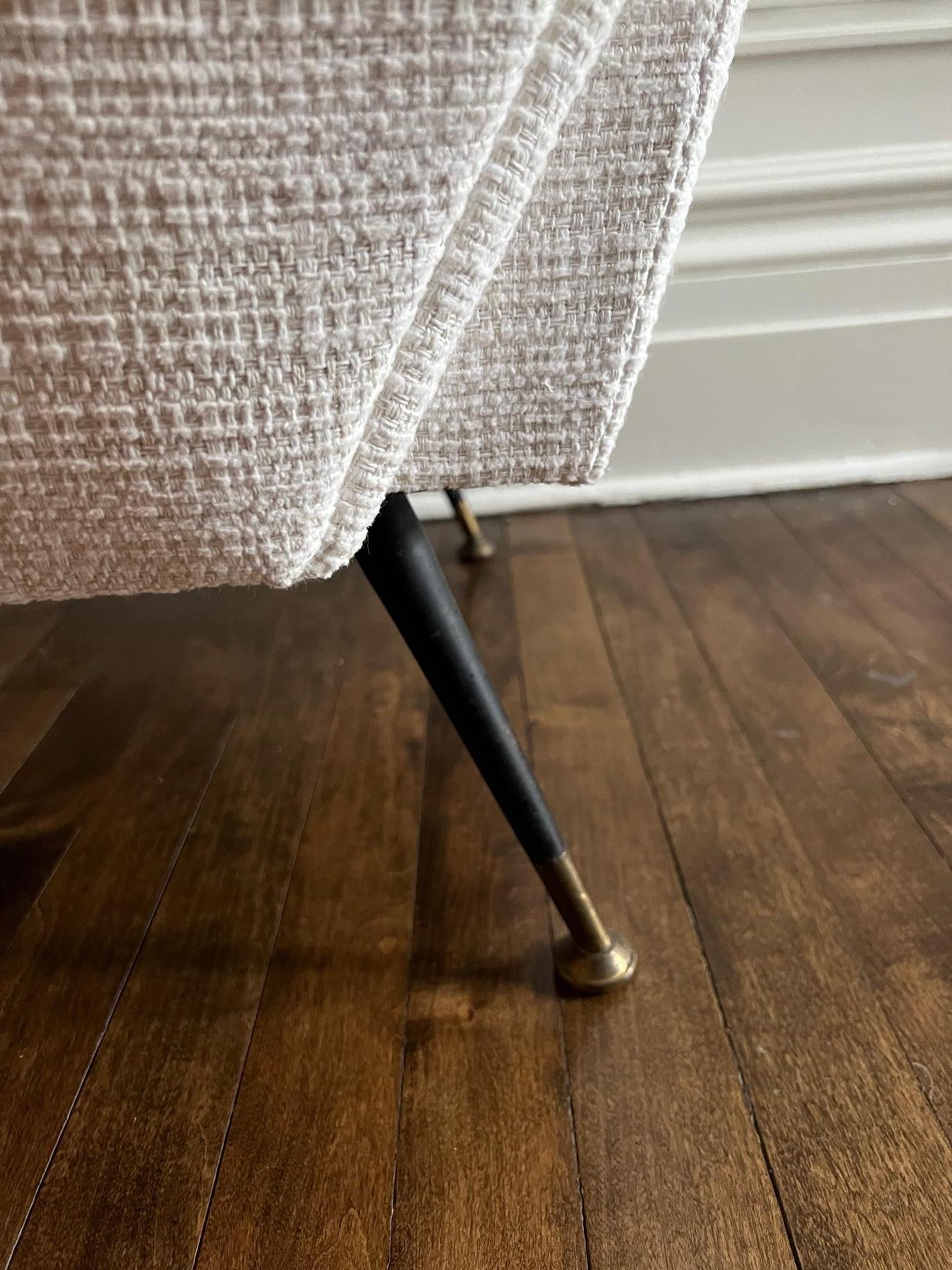 A pair of mid-20th Century armchairs. These chairs have a steel base and brass footrest. They are newly upholstered in a cream performance fabric that has a textures as shown. Incredibly durable (even red wine is cleanable) it is very elegant and