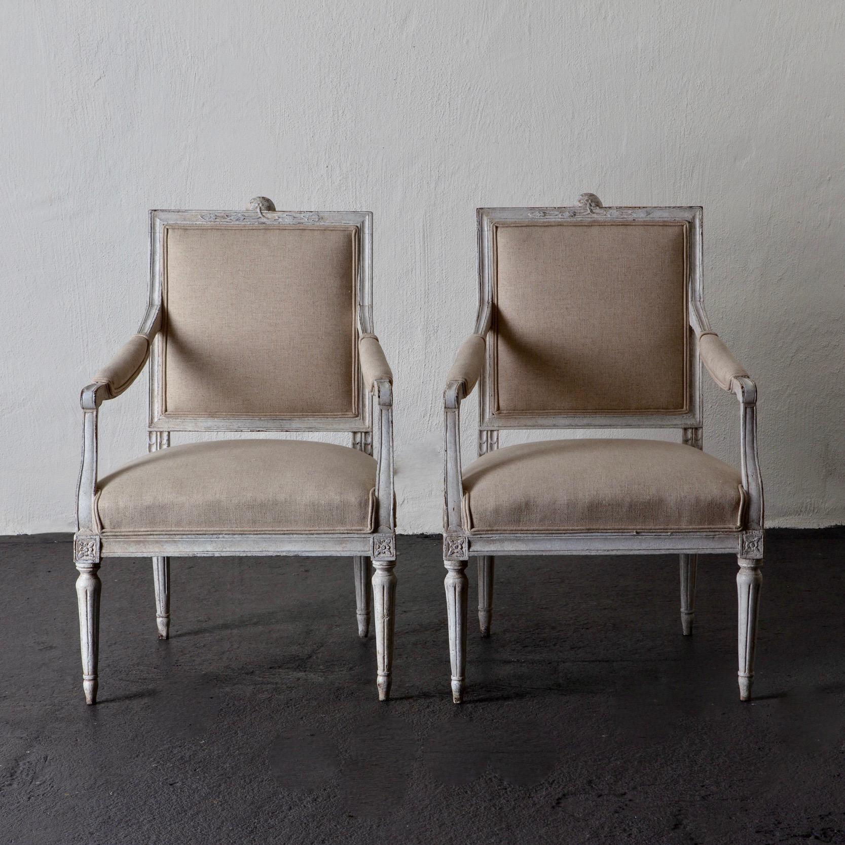 Armchairs pair of Swedish Gustavian, 1790-1810 white beige, Sweden. A pair of armchairs made during the Gustavian period in Sweden. The wooden frame painted in a distressed white finish. Beautiful carvings. Upholstered in a beige linen fabric.