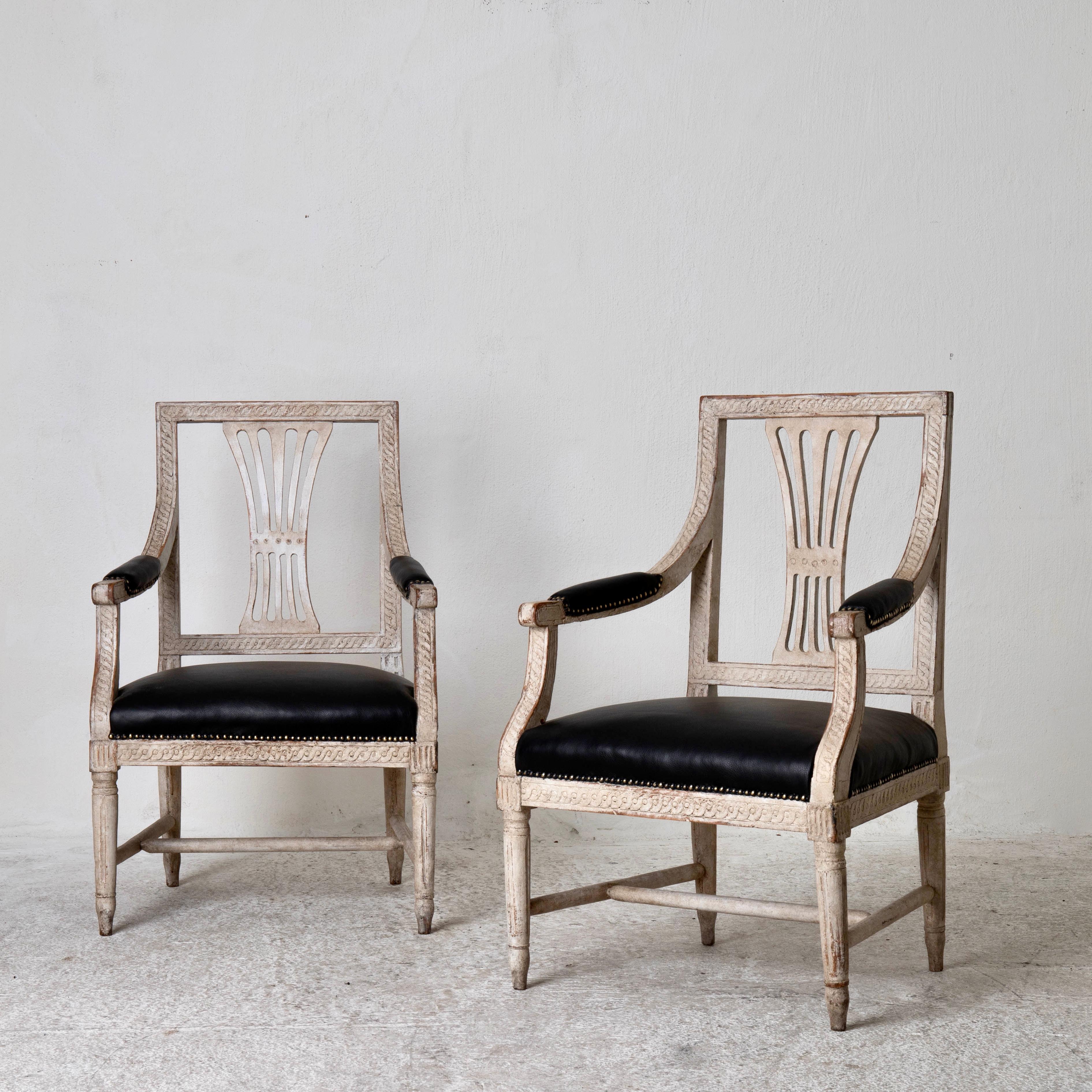 Armchairs Swedish Gustavian period white Sweden. A pair of armchairs made during the Gustavian period in Sweden. Distressed white finish and upholstered in a black leather, Armrests semi upholstered, Frame carved with a ribbon and rounded legs