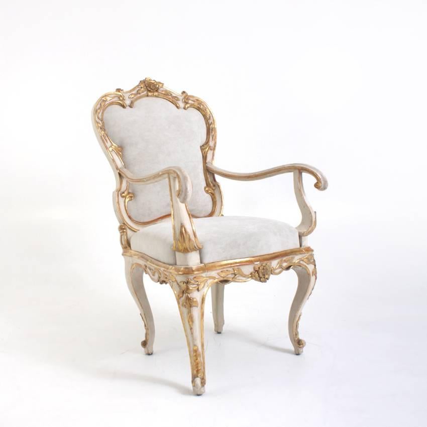 Pair of Italian armchairs on capriole legs with elegant curved armrests and scalloped backrests. The chairs are painted in a crème-white and decorated with gilt c-buckles and rose ornaments.