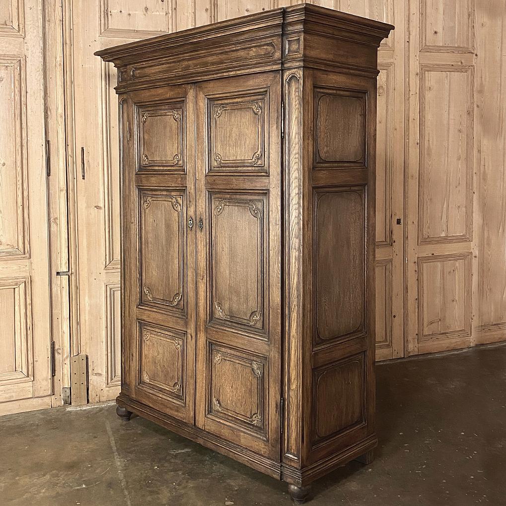 19th century country French Louis XIV Armoire is a study in architectural purity, with raised and recessed molded panels adorning the doors, accented with Minimalist carvings on the corners of the panels for just a bit of visual intrigue. Original