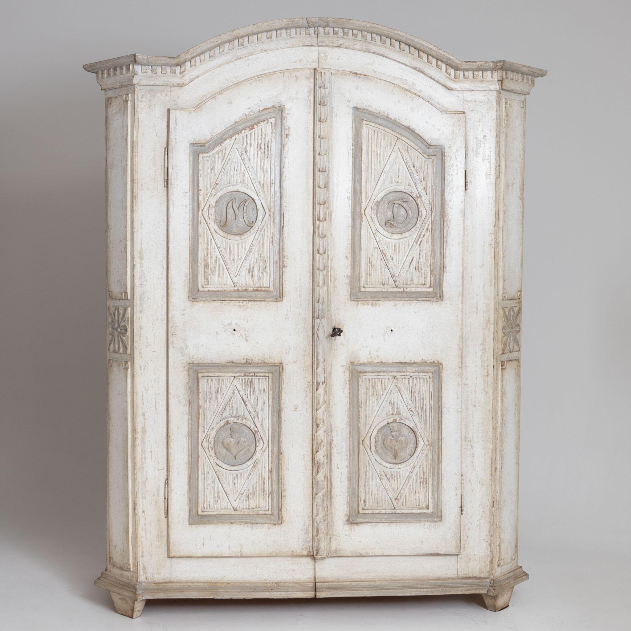 Cream and white painted armoire with rounded cornice with dentil frieze and filling fields on the front with initials M D and burning hearts. The modern interior division with clothes rail, shelves and two drawers.