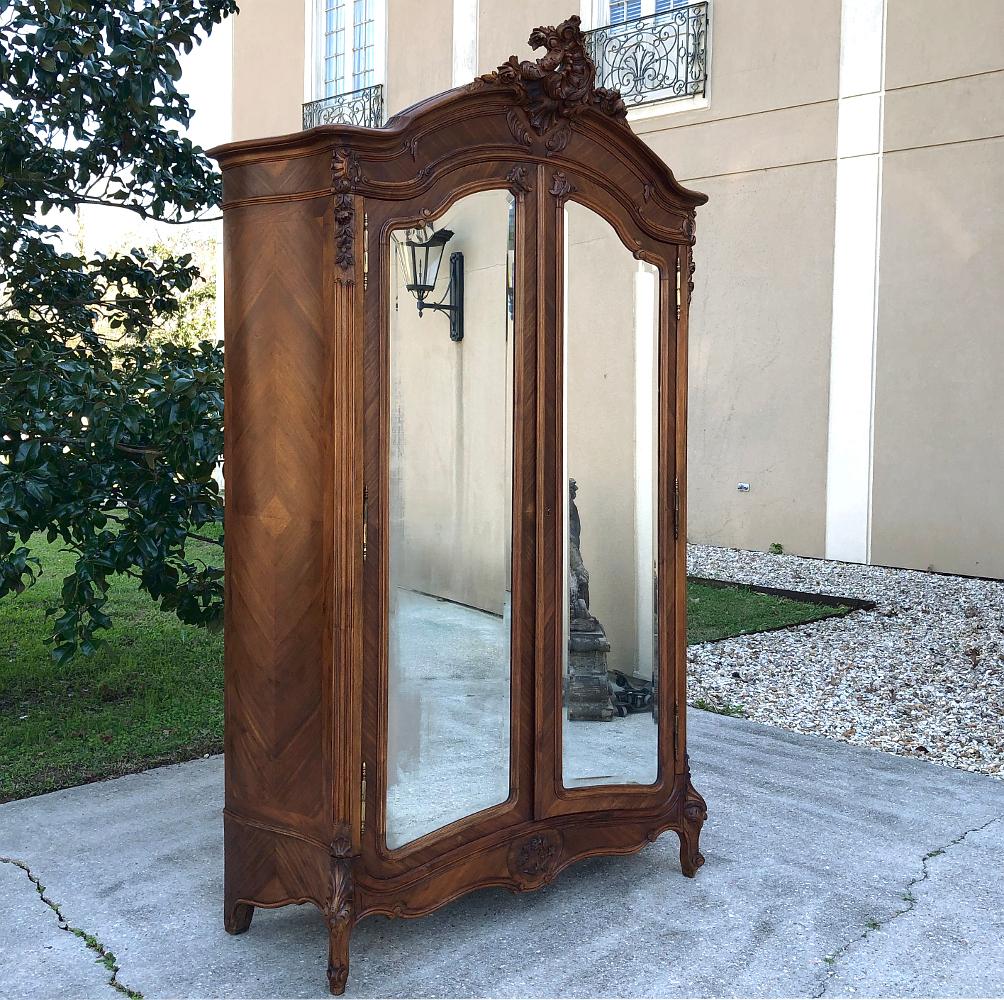19th century French Louis XV walnut armoire exudes the Classic lines of the rococo movement, with asymmetrical shell, floral and foliate carving atop the boldly arched crown. The scrollwork and exquisite carved embellishment of the apron and legs