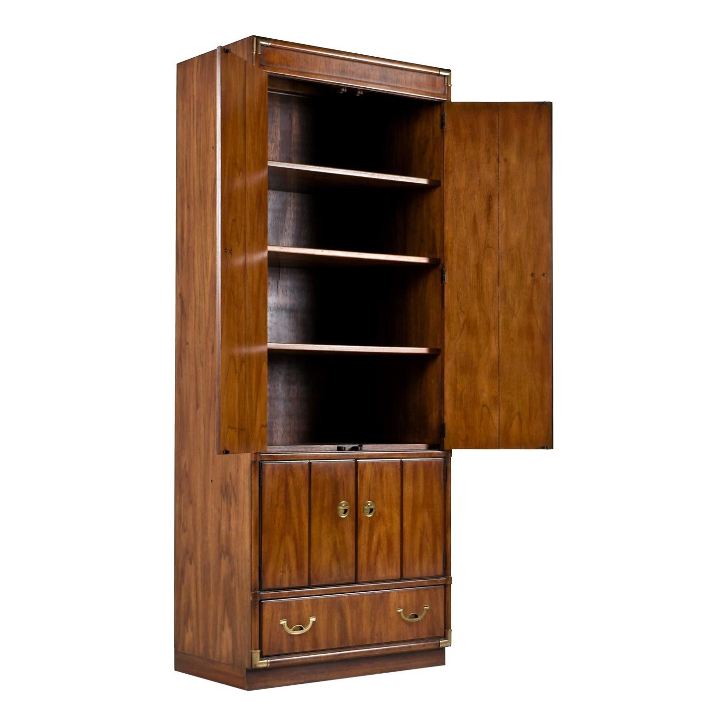 Solid wood Campaign style corner cabinet curio bookshelf made by esteemed US furniture maker Drexel Heritage in the 1970s. Faux bamboo brass corner accents on all four corners and brass pull hardware tie together British traditional and Eastern