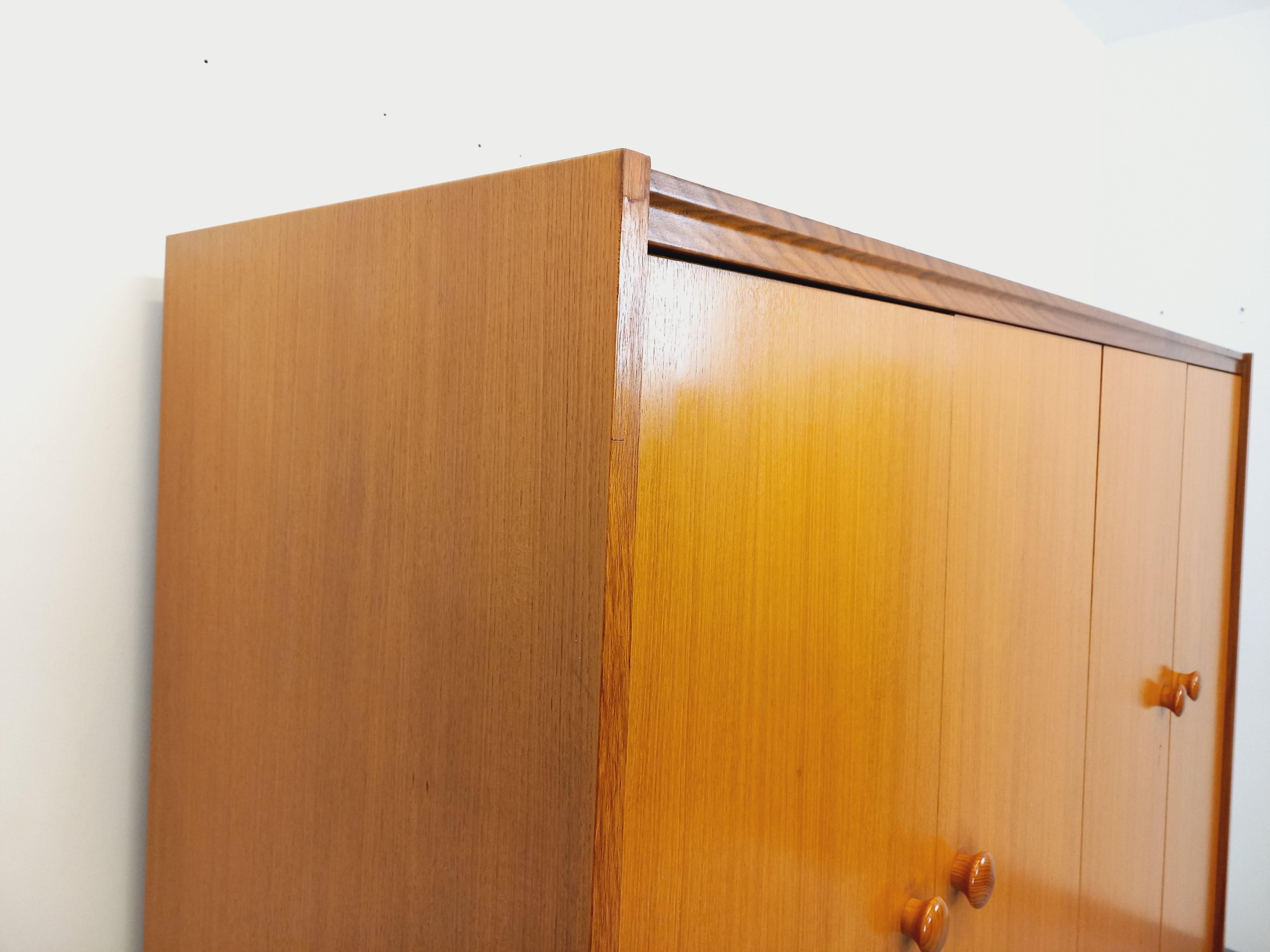 Armoire dressing vintage style moderniste des années 60 70, en teck et Noyer, sur plinthe, jolies poignées, 4 portes, beaucoup de rangements : 1 partie avec étagère et penderie, 1 partie avec grande étagère, 3 tiroirs. Très bon état général avec