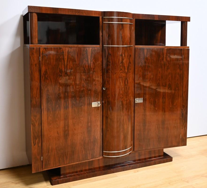 Questo armadio impiallacciato in noce, risalente all'epoca Art Déco degli anni '30, è un vero capolavoro di design e funzionalità.
Si distingue per le sue tre porte, di cui quella centrale è curva e messa in risalto da un'elegante striscia di