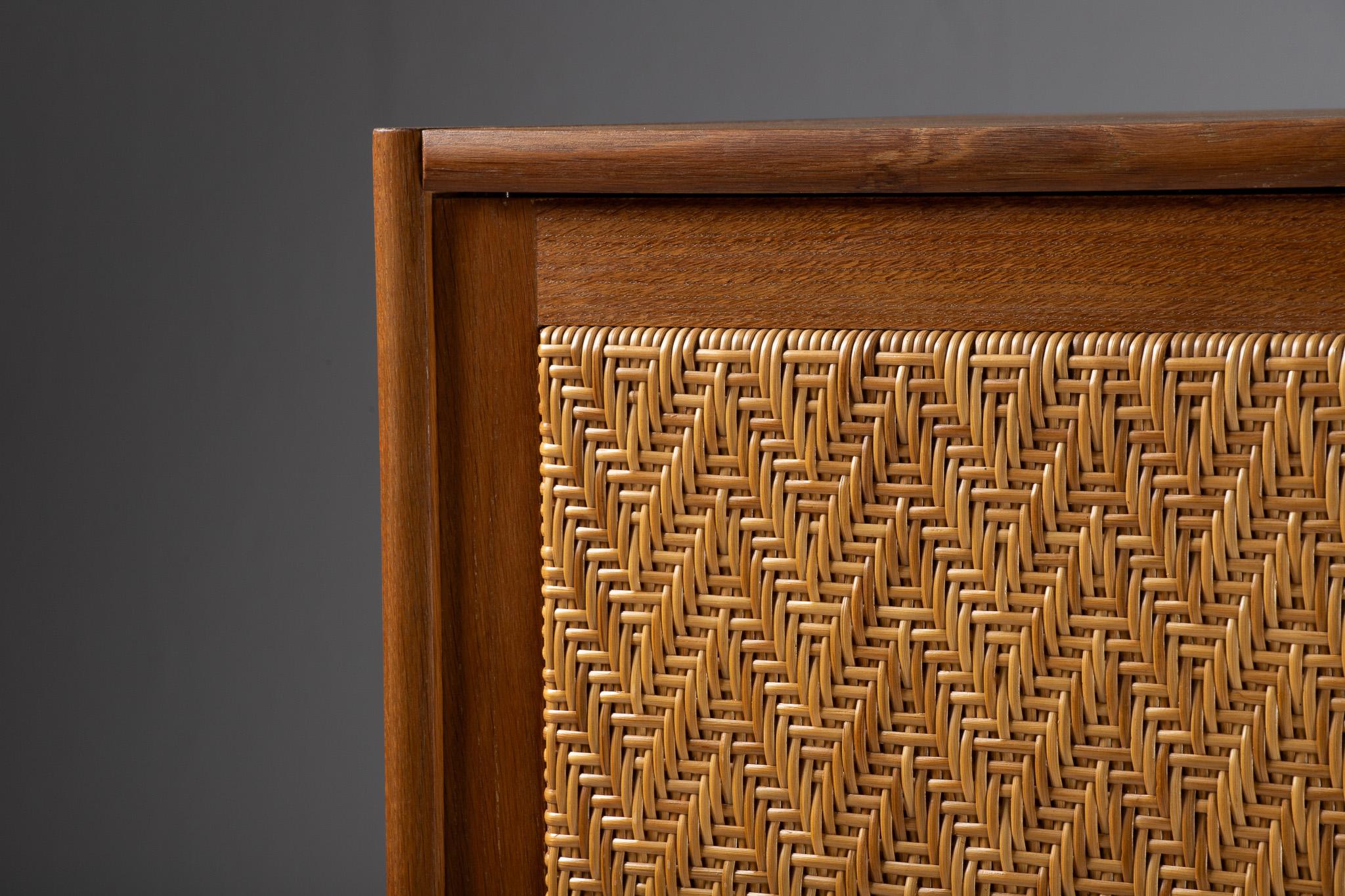 A study in restraint and texture, this tall, singular armoire rises like a quiet monolith—its façade defined by a single woven plane set flush within a clean teak frame. The silhouette is austere, but the material language is tactile and luminous: a