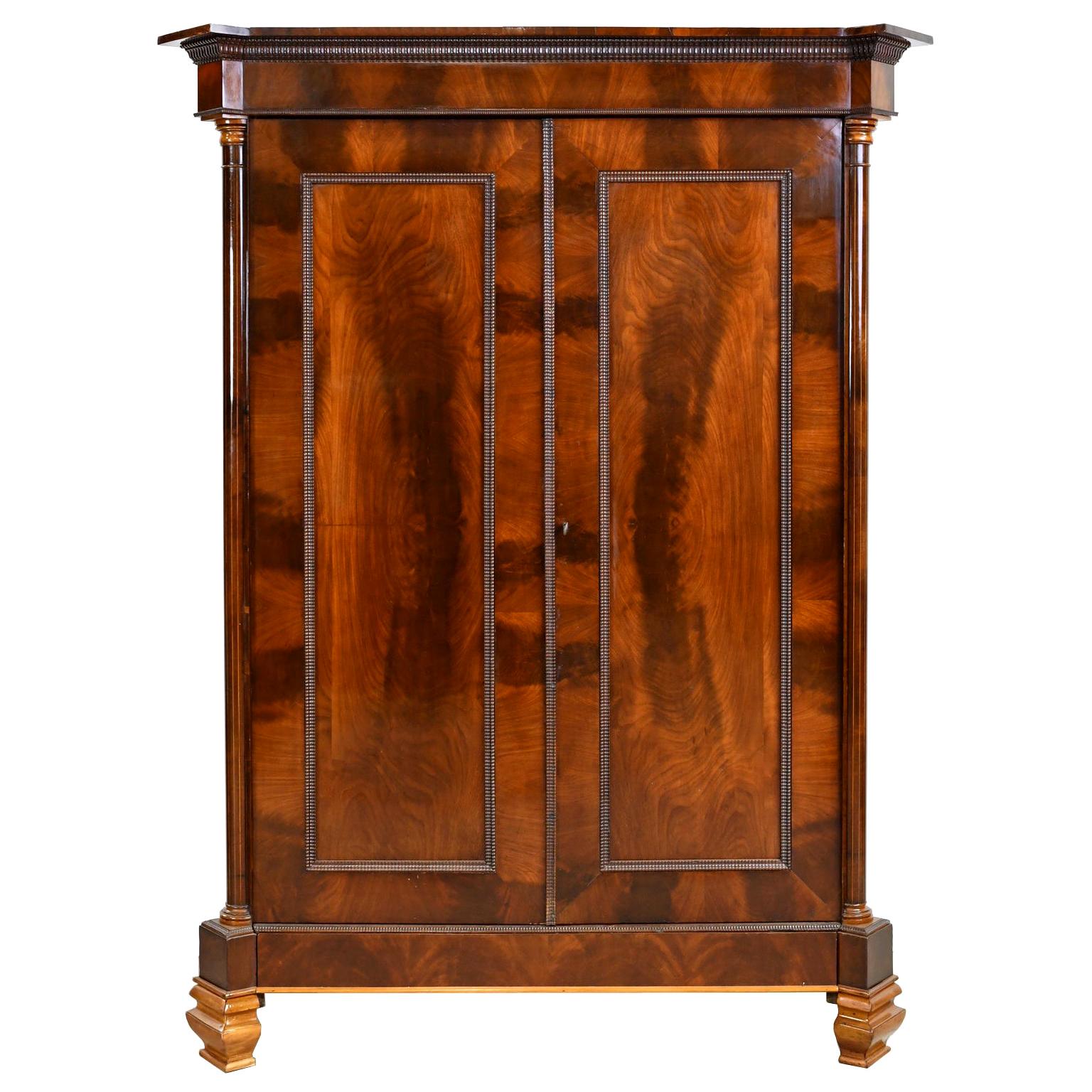 An exquisite armoire in West Indies mahogany with fine book-matching throughout accentuating the beautiful figuring of this choice wood's grain. On the chamfered corners are turned mahogany columns with fine line inlays of satinwood that flank two